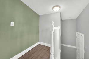 Stairwell landing featuring a white painted balustrade, wood-finish flooring, a contemporary flush mount light fixture, and a paneled interior door