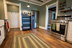 Gourmet kitchen featuring stainless steel appliances, wood-finish flooring, white cabinetry, and a farmhouse sink