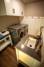Laundry area featuring wood-finish flooring, white shaker cabinetry with dark hardware, and a board and batten wall treatment