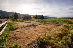 Expansive land parcel featuring open terrain, a rustic wooden fence, mountainous backdrop, and distant structures