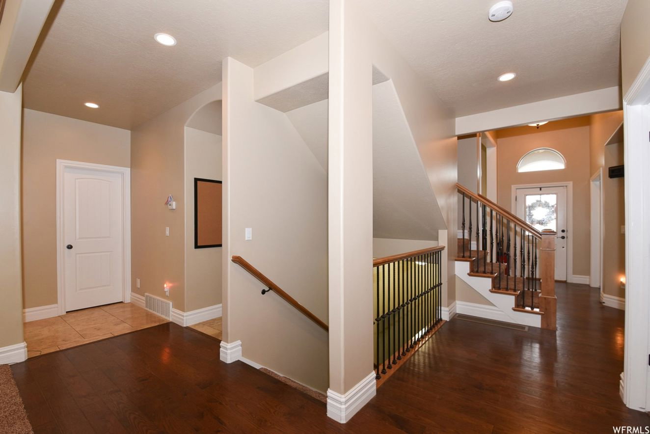 Foyer showcasing a wood-finish flooring, a staircase with wood handrails and wrought iron balusters, recessed lighting, and an arched entry with a transom window