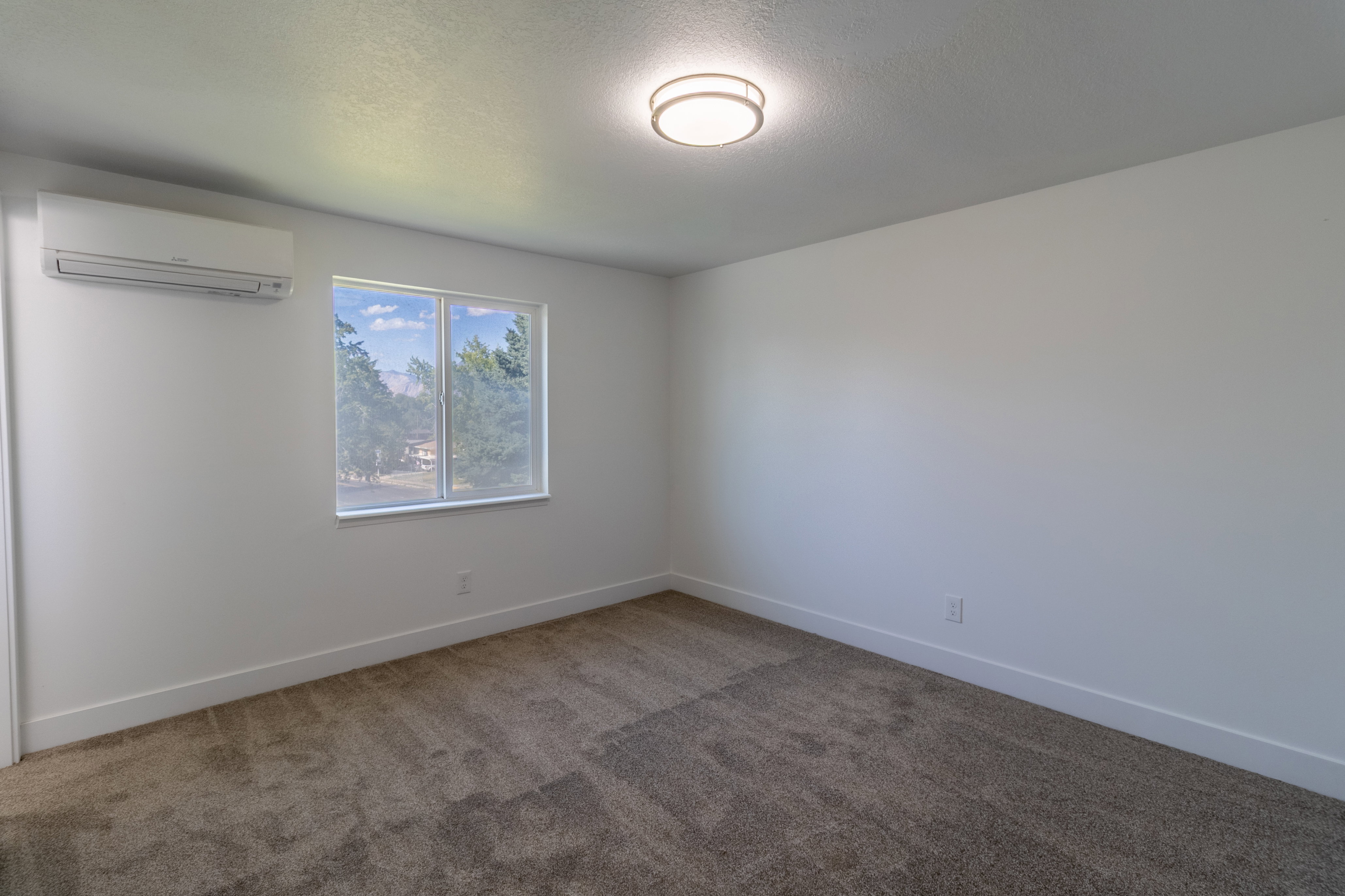 Neutral white walls featuring a window with exterior scenery, a wall-mounted mini-split unit, a contemporary ceiling light fixture, and textured carpeting