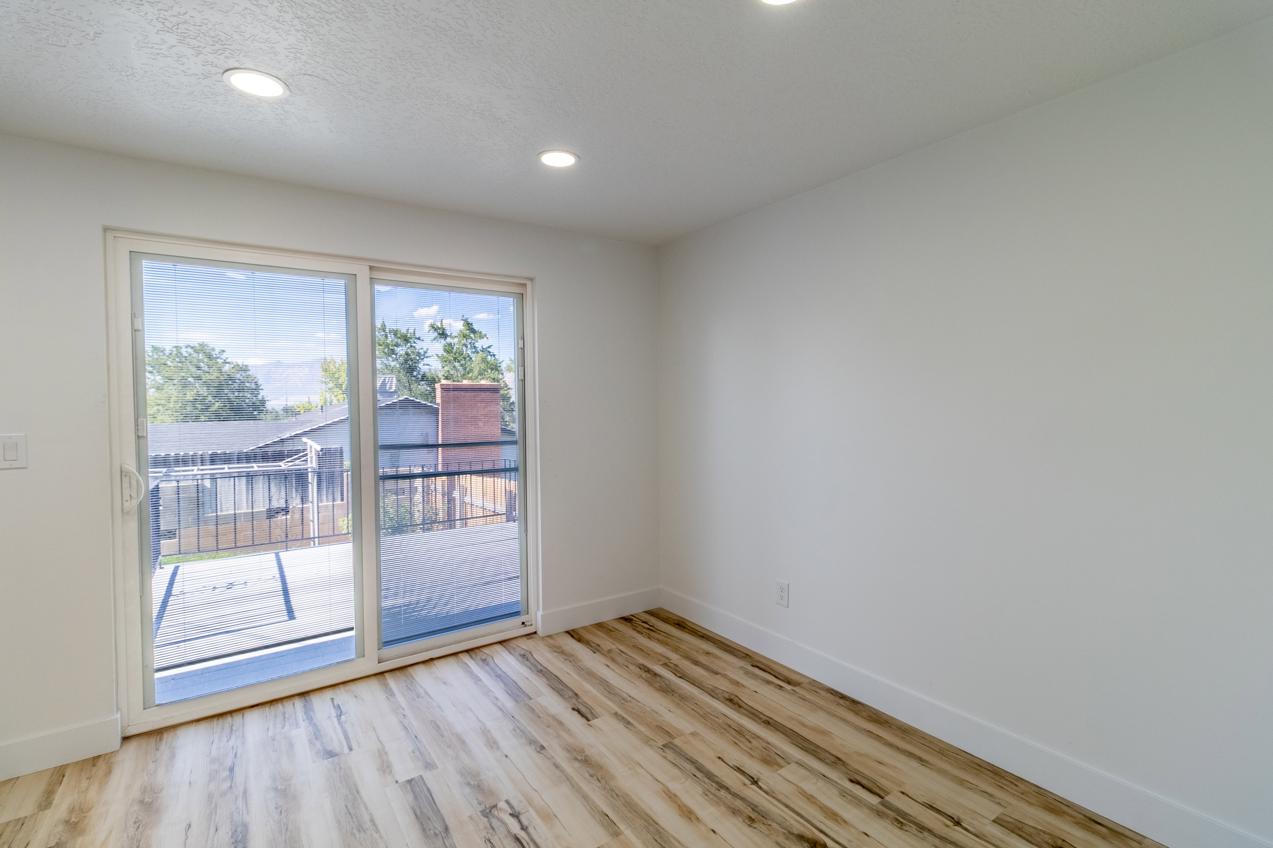 Light-filled interior space featuring wood-finish flooring, recessed lighting, and a sliding glass door leading to an exterior balcony