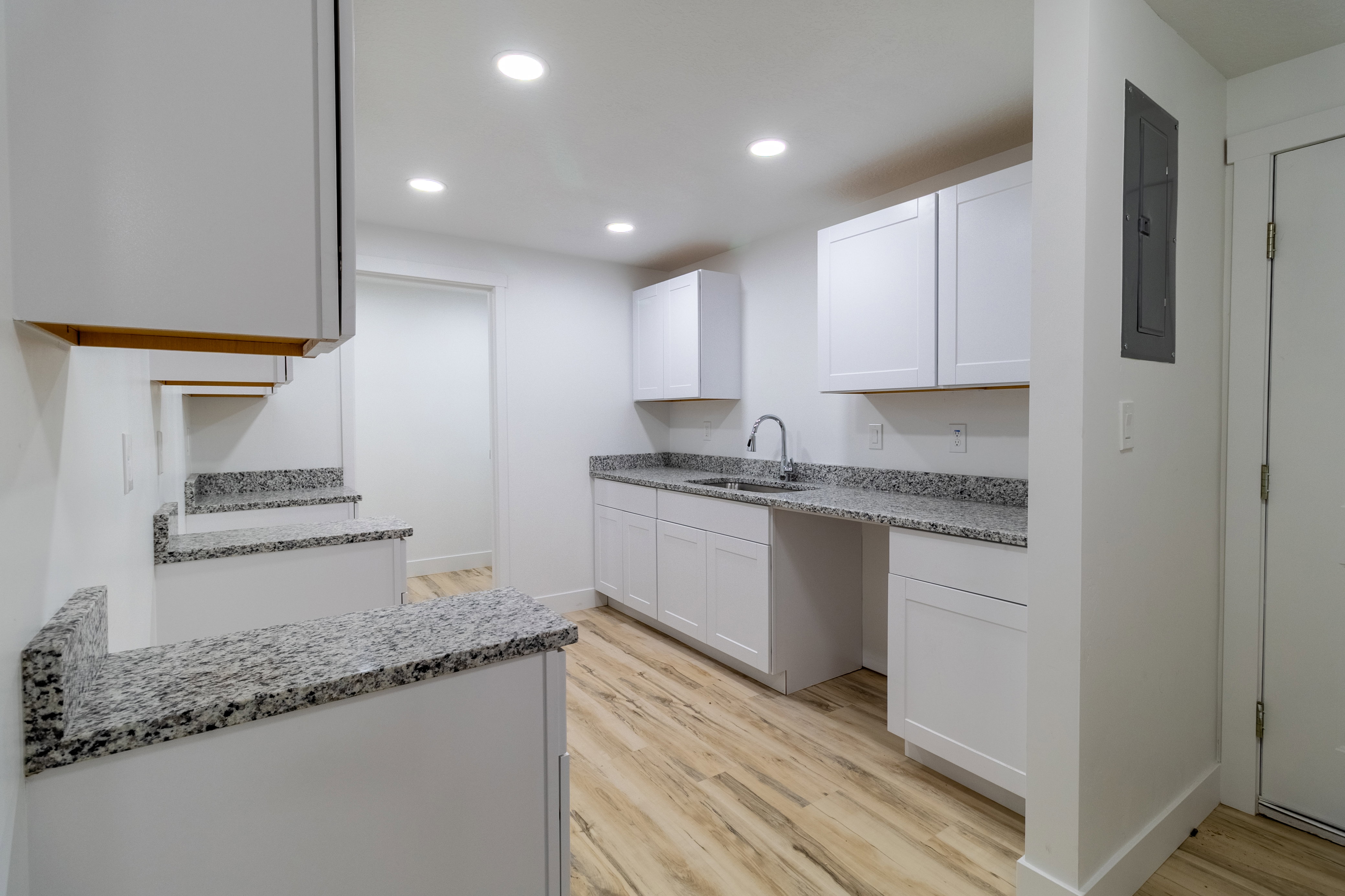 Kitchenette featuring wood-finish flooring, white cabinetry, granite-finish countertops, stainless steel sink, and recessed lighting