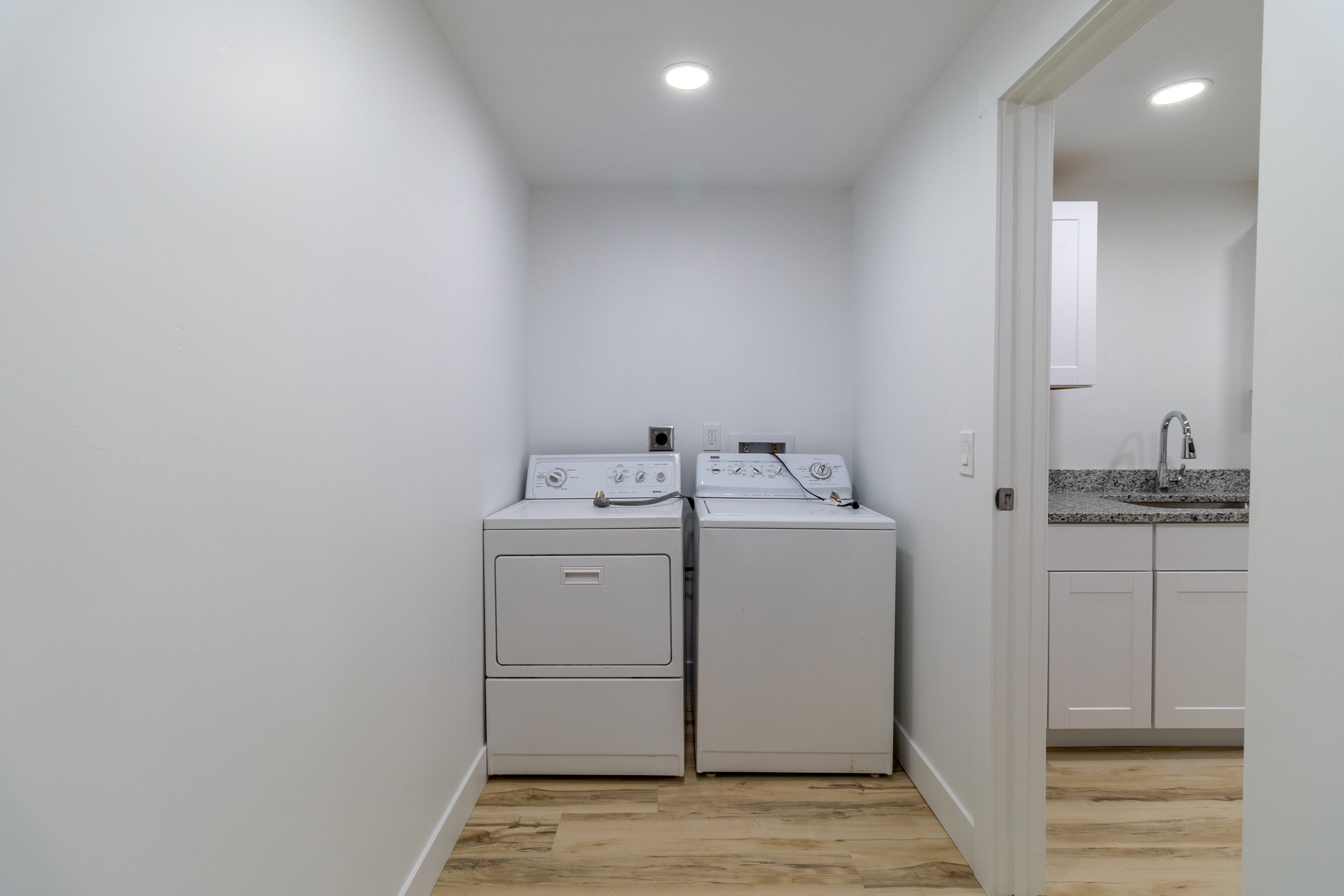 Dedicated laundry area featuring wood-finish flooring, recessed lighting, and a white appliance set