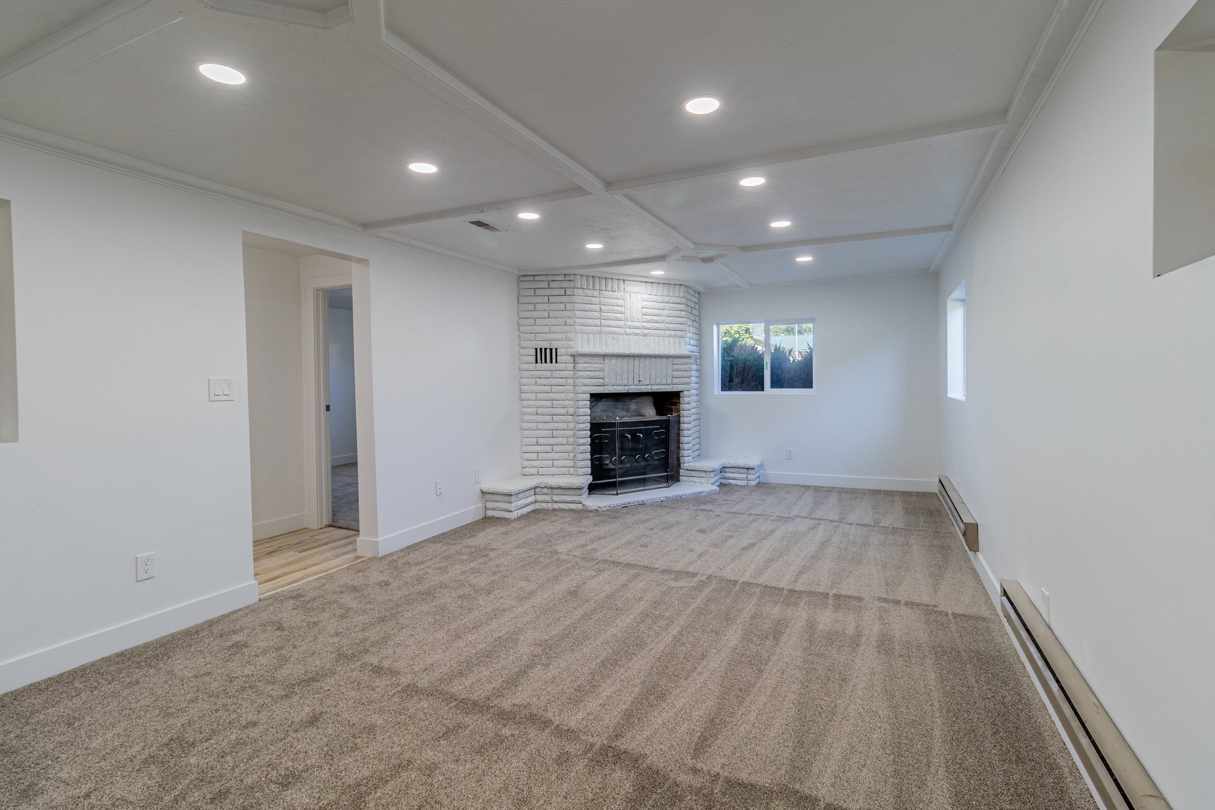 Spacious room featuring a white painted brick fireplace with a black insert, recessed lighting, and a coffered ceiling