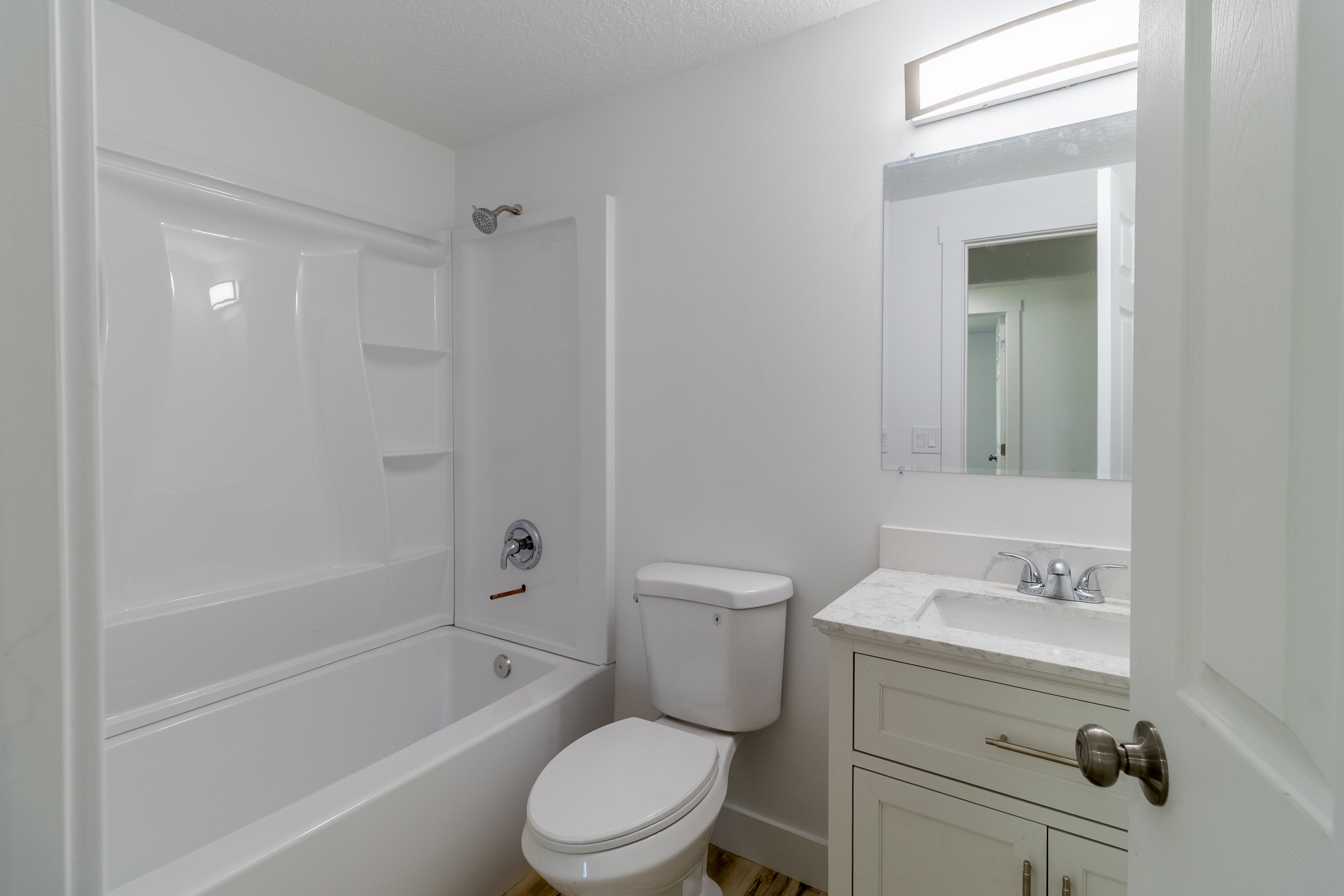 White bathroom featuring a built-in tub and shower unit, a vanity with a stone-finish countertop, a single basin sink, and a chrome faucet
