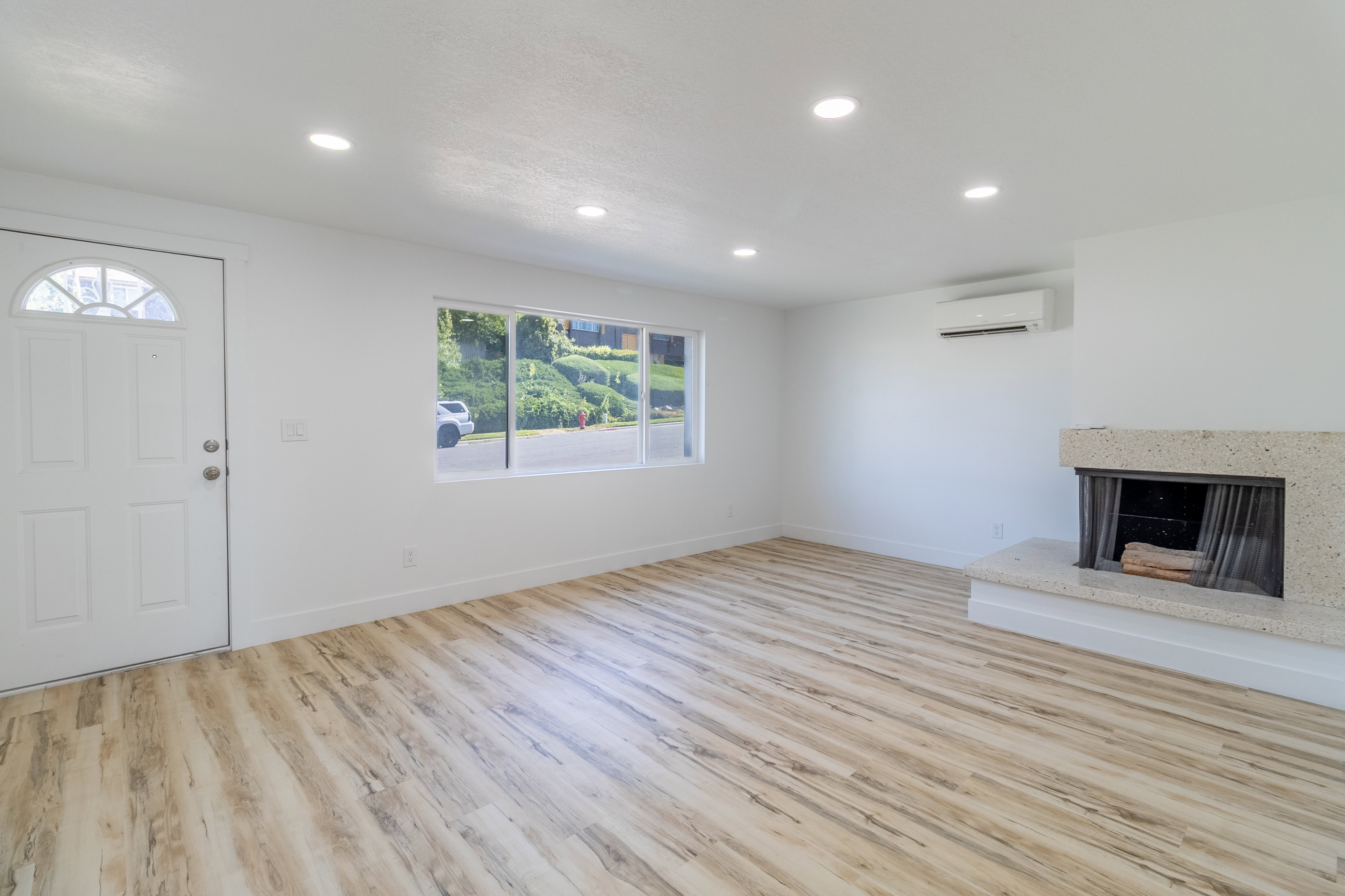 Spacious living area featuring wood-finish flooring, a stone fireplace, recessed lighting, and a ductless mini-split system