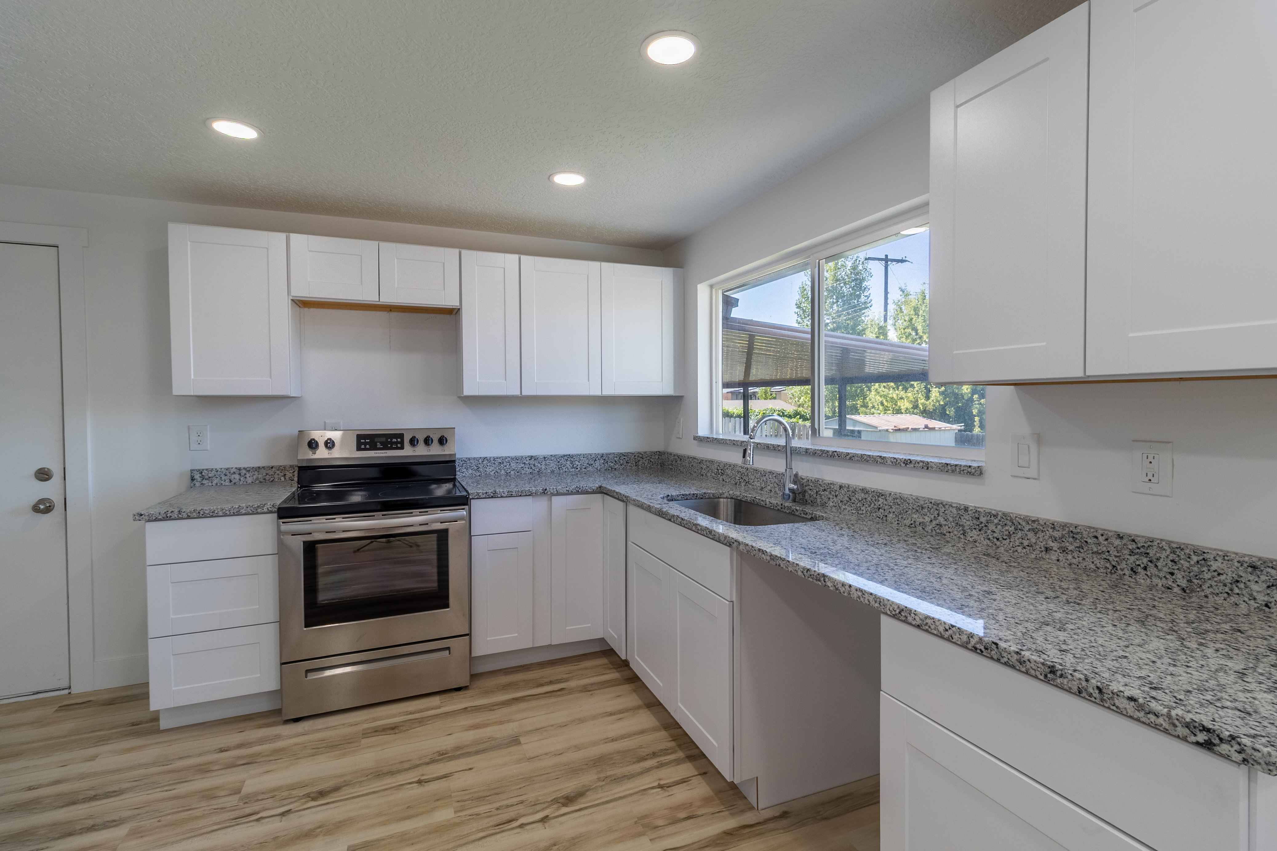 Modern kitchen featuring white shaker cabinetry, speckled countertops, stainless steel appliances, and wood-finish flooring