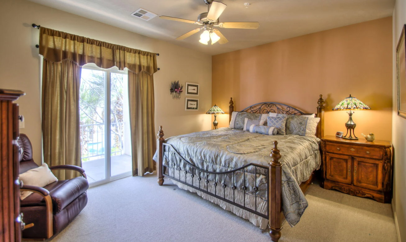 Carpeted bedroom with a ceiling fan, sliding glass door balcony access, and a metal bed frame