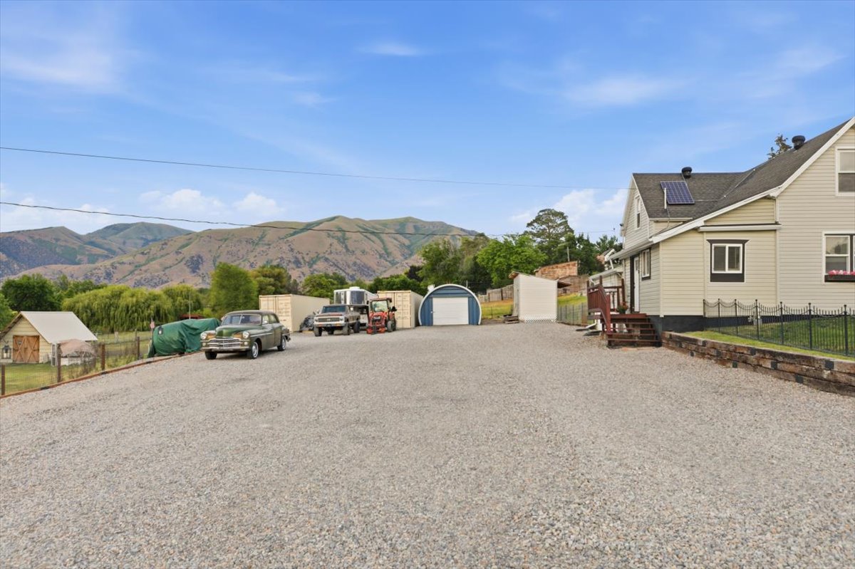 Expansive gravel parking area with a separate storage shed, a blue quonset hut, and a small outbuilding