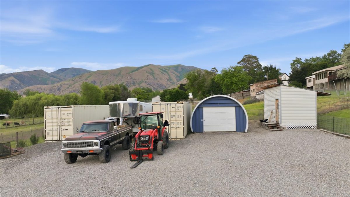 Expansive gravel lot featuring multiple storage containers, a blue arched garage with a white roll-up door, and an additional white shed