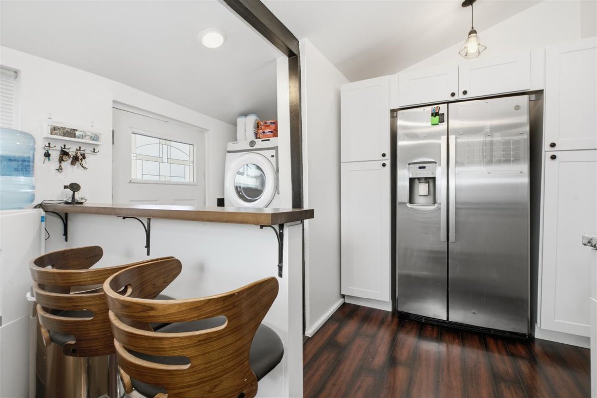White cabinetry and a stainless steel side-by-side refrigerator complement wood-finish flooring