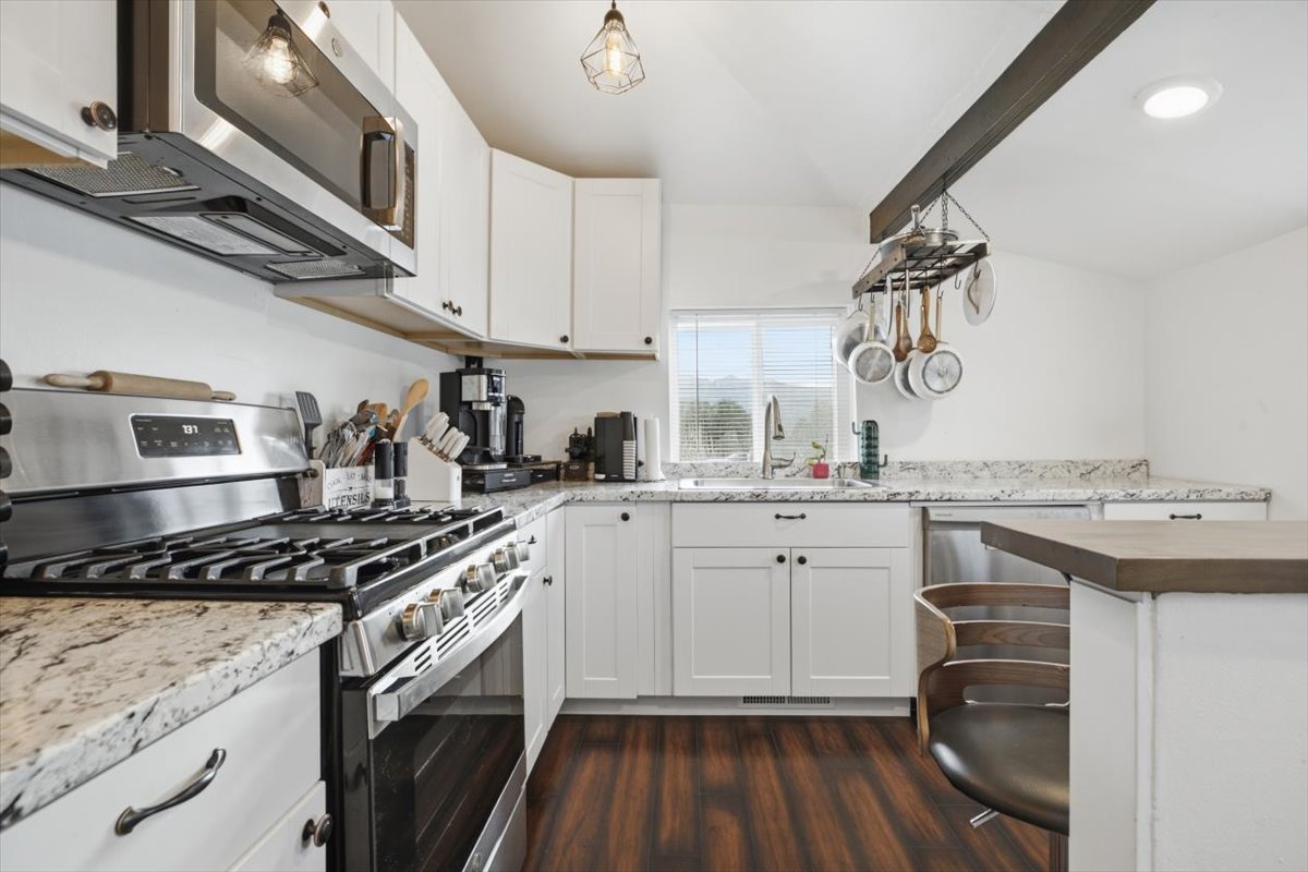 Kitchen featuring white cabinetry, stainless steel appliances, speckled countertops, wood-finish flooring, and a breakfast bar