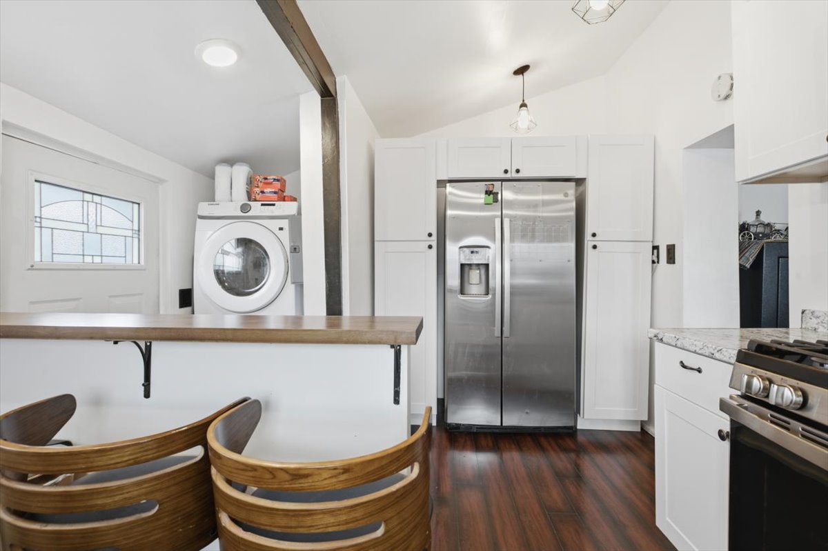Modern kitchen featuring white cabinetry, stainless steel appliances, wood-finish flooring, and a breakfast bar with a solid surface countertop