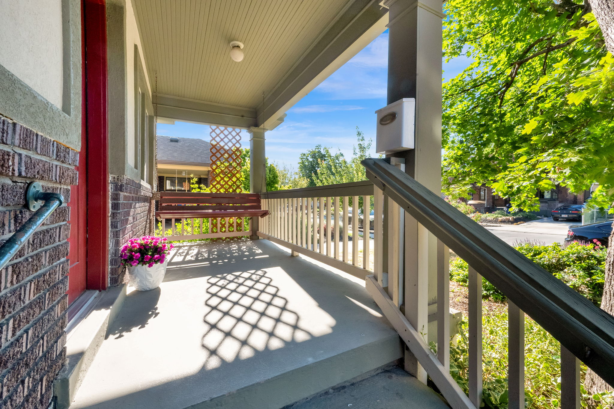 Inviting covered porch featuring a red entry door, brick siding, a wood-finish porch swing, and a decorative trellis