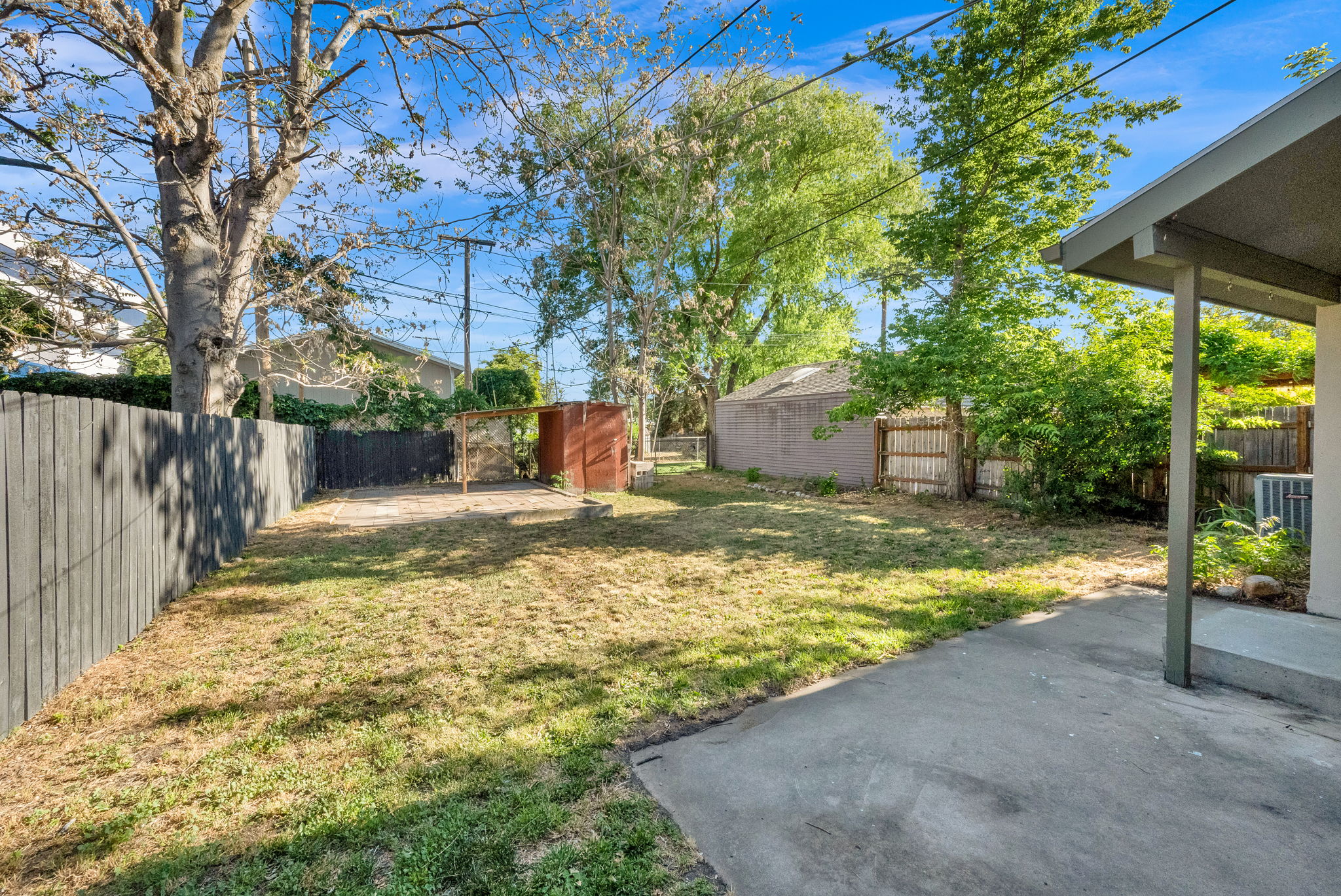 Expansive backyard featuring a concrete patio, a wood privacy fence, mature trees, and a detached shed