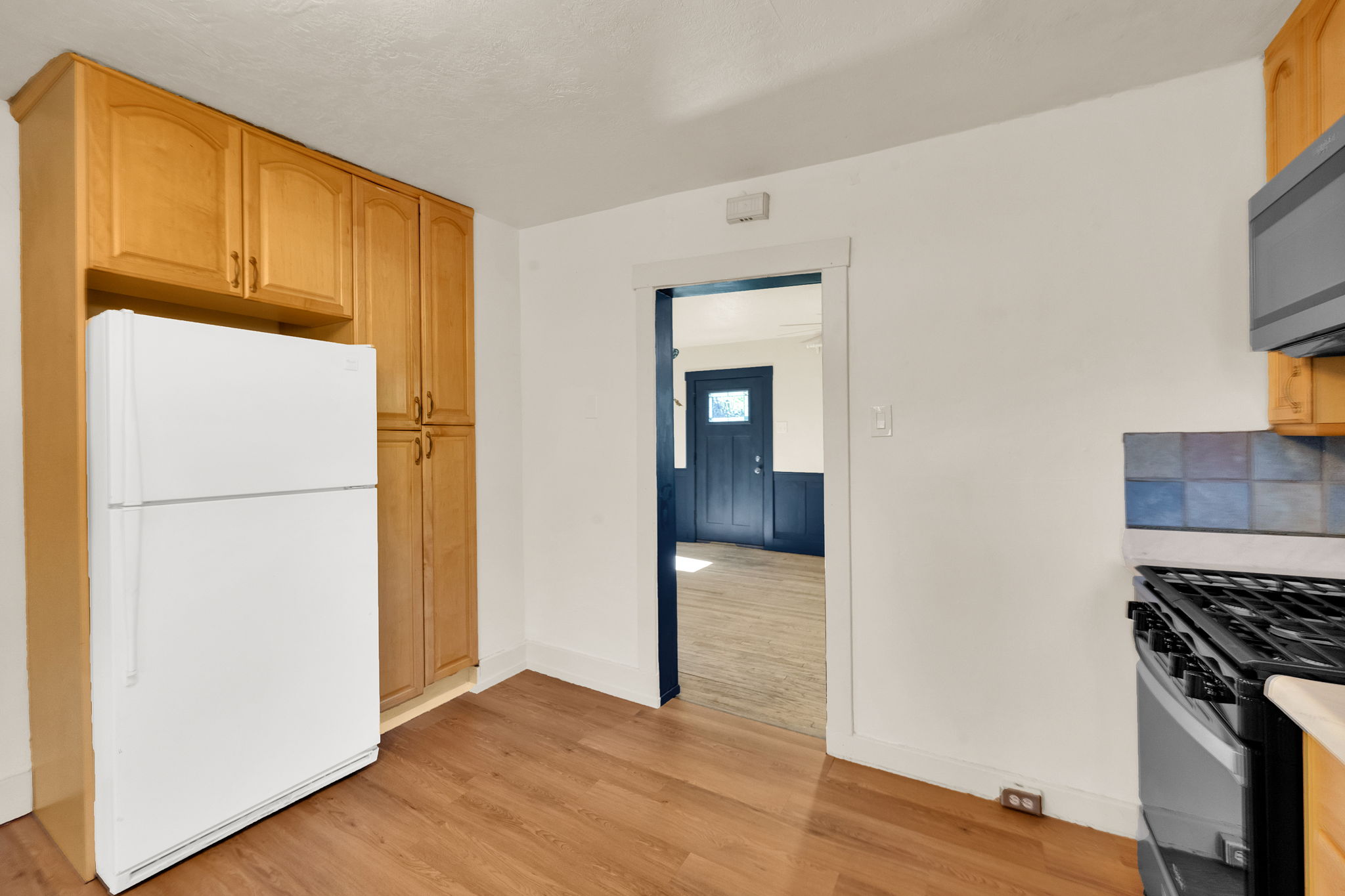 Wood-finish flooring, light wood cabinetry, and a gas range with tiled backsplash