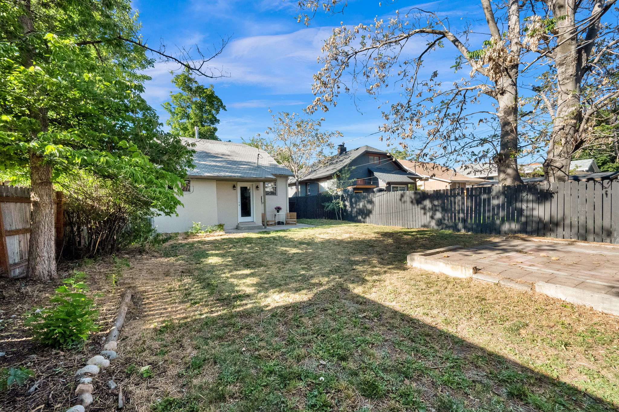 Spacious backyard featuring a grass lawn, mature trees, a privacy fence, and a concrete paver patio