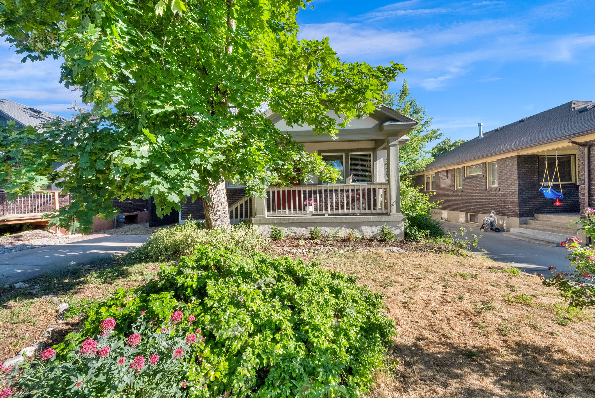 Craftsman-style home featuring a covered front porch with white railing, framed by mature trees and established landscaping