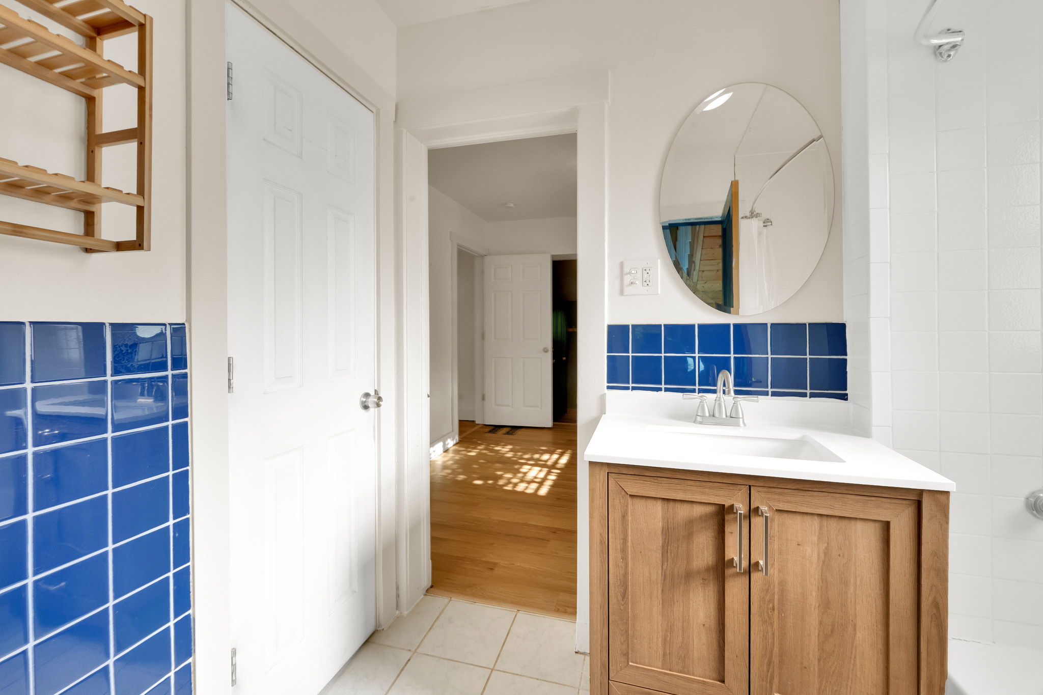Bathroom featuring a wood-finish vanity with a white countertop and integrated sink, a circular mirror, and blue tile wainscoting