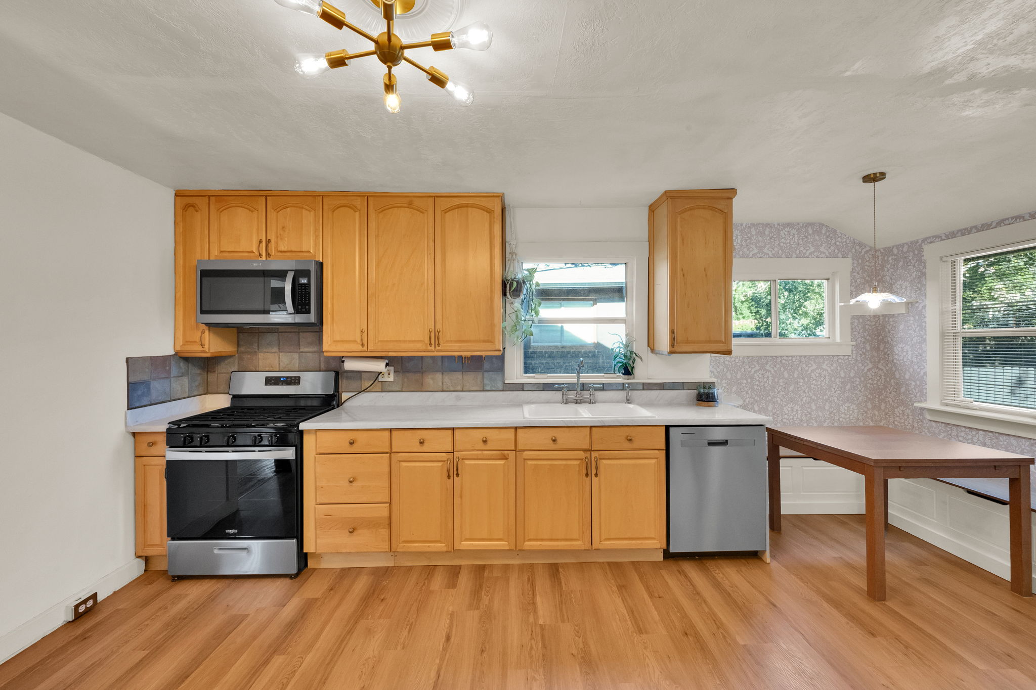 Kitchen featuring wood-finish flooring, light wood cabinetry, stainless steel appliances, and a tiled backsplash