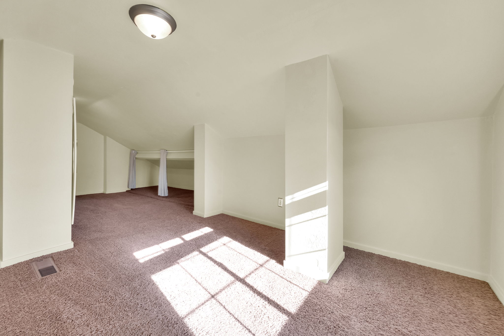 Spacious interior featuring sloped ceilings, plush carpeting, recessed alcoves, a flush-mount ceiling light, and white baseboards
