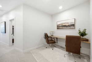 Dedicated workspace featuring a built-in wood-finish desk, recessed lighting, and soft carpeting