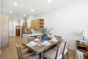 Open-concept living space featuring wood-finish flooring, a contemporary kitchen with light-toned cabinetry, a large kitchen island with a basin sink, stainless steel appliances, and a wood entry door with frosted glass