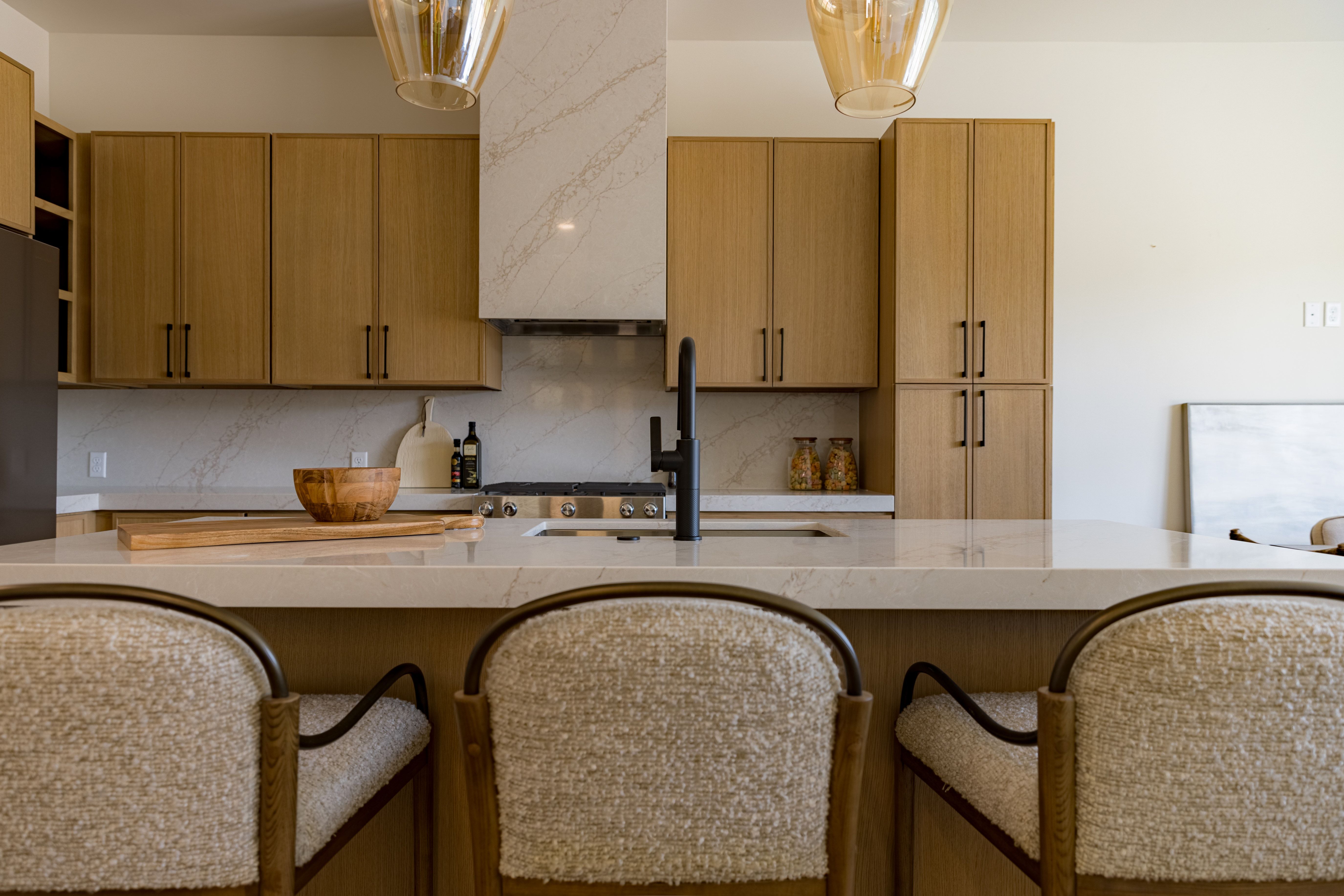 Gourmet kitchen featuring a waterfall island with a double basin sink, light wood-finish cabinetry, a stainless steel range, and an integrated hood vent