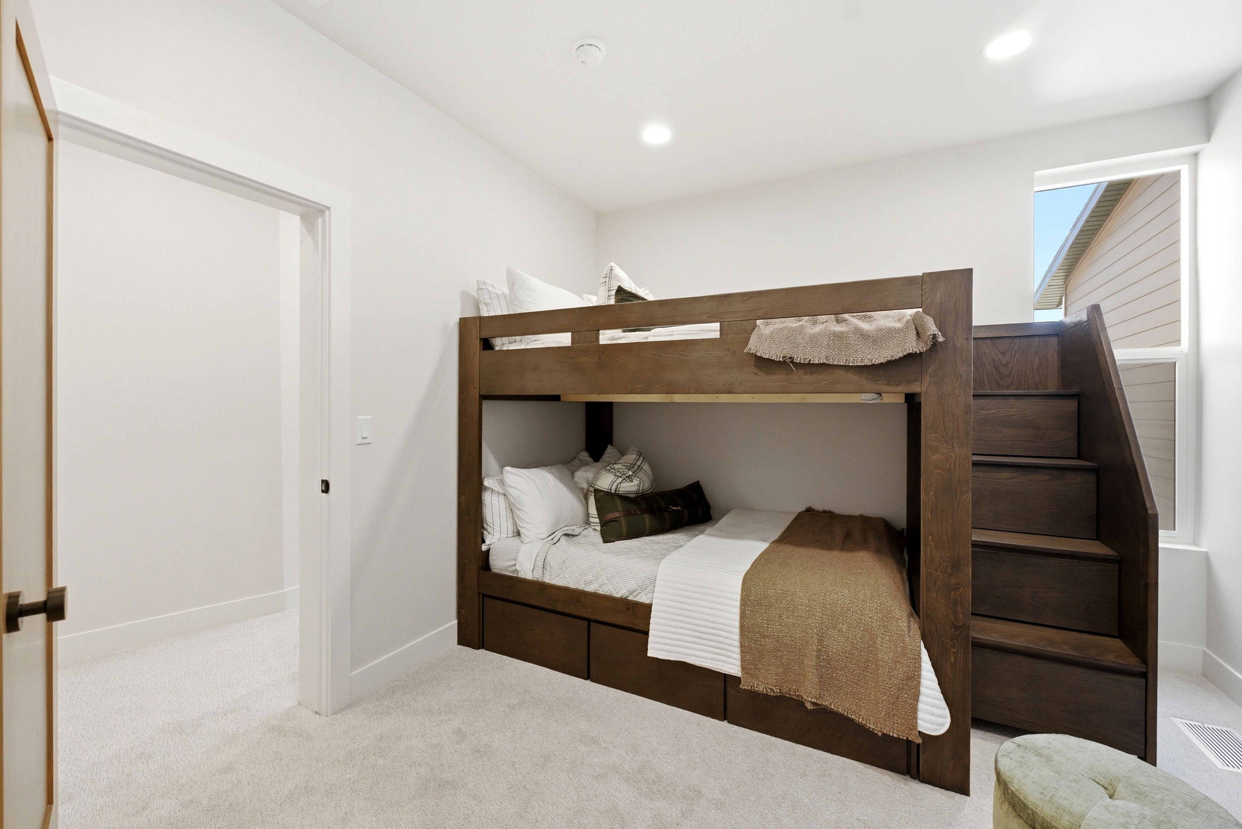 Built-in wood-finish bunk beds featuring integrated storage drawers and a staircase entry