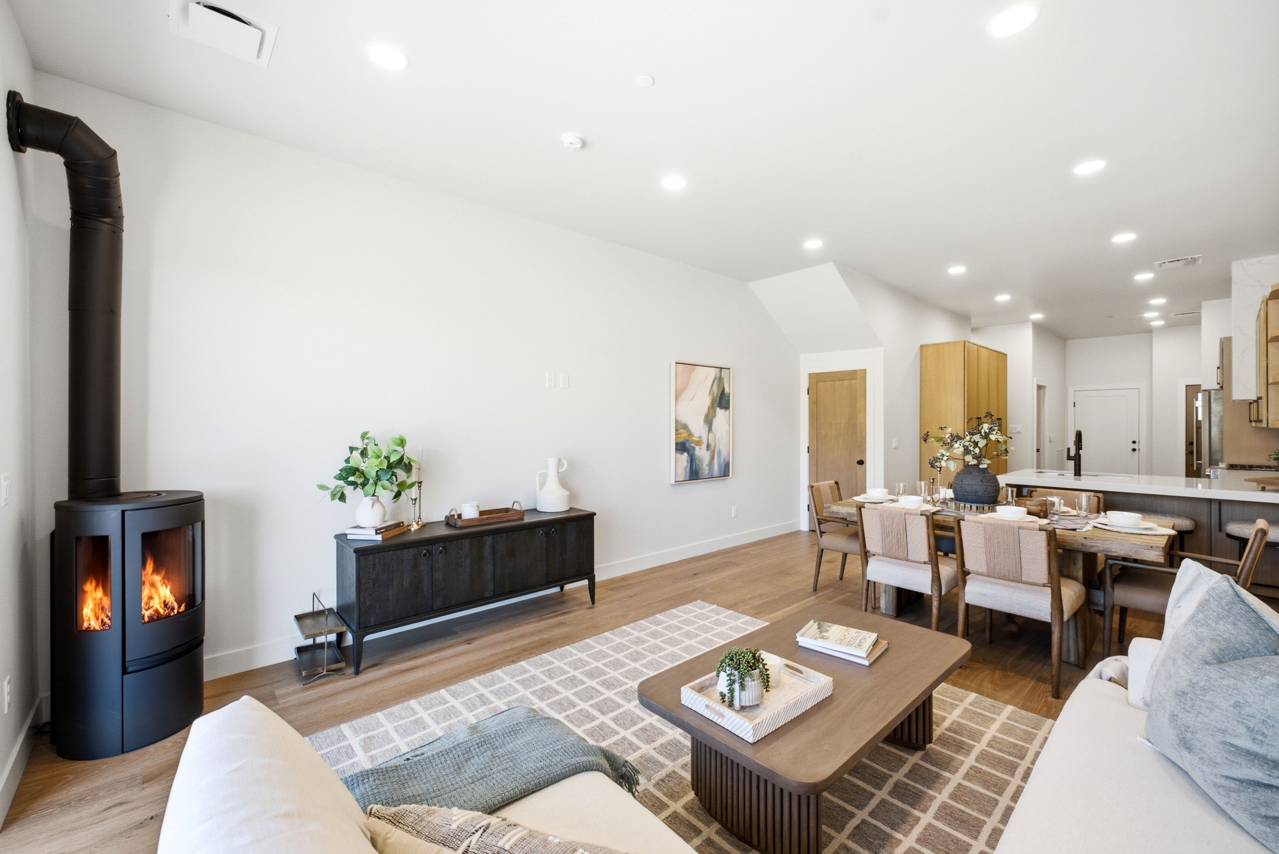 Open-concept living space featuring a freestanding fireplace with visible flame, light wood-finish flooring, recessed lighting, and a vaulted ceiling