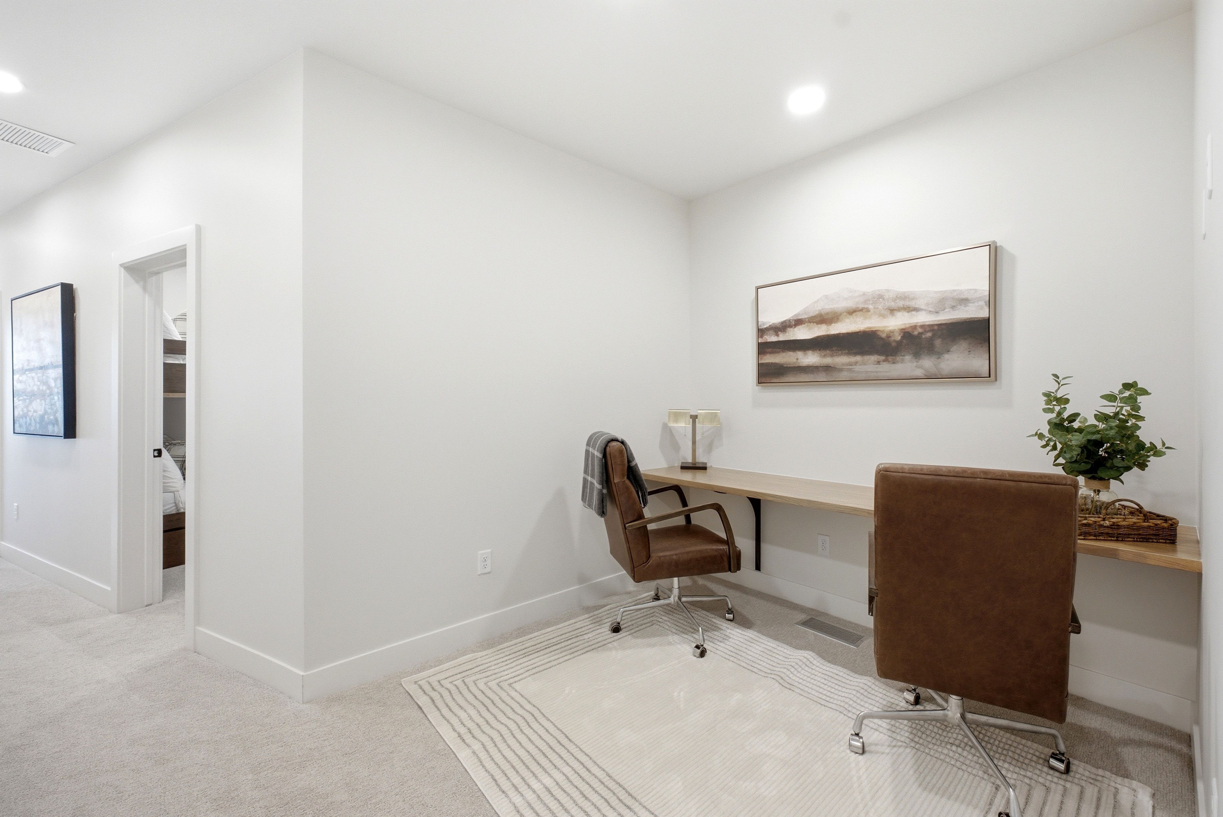 Dedicated workspace featuring a built-in wood-finish desk, recessed lighting, light gray walls, and plush carpet flooring