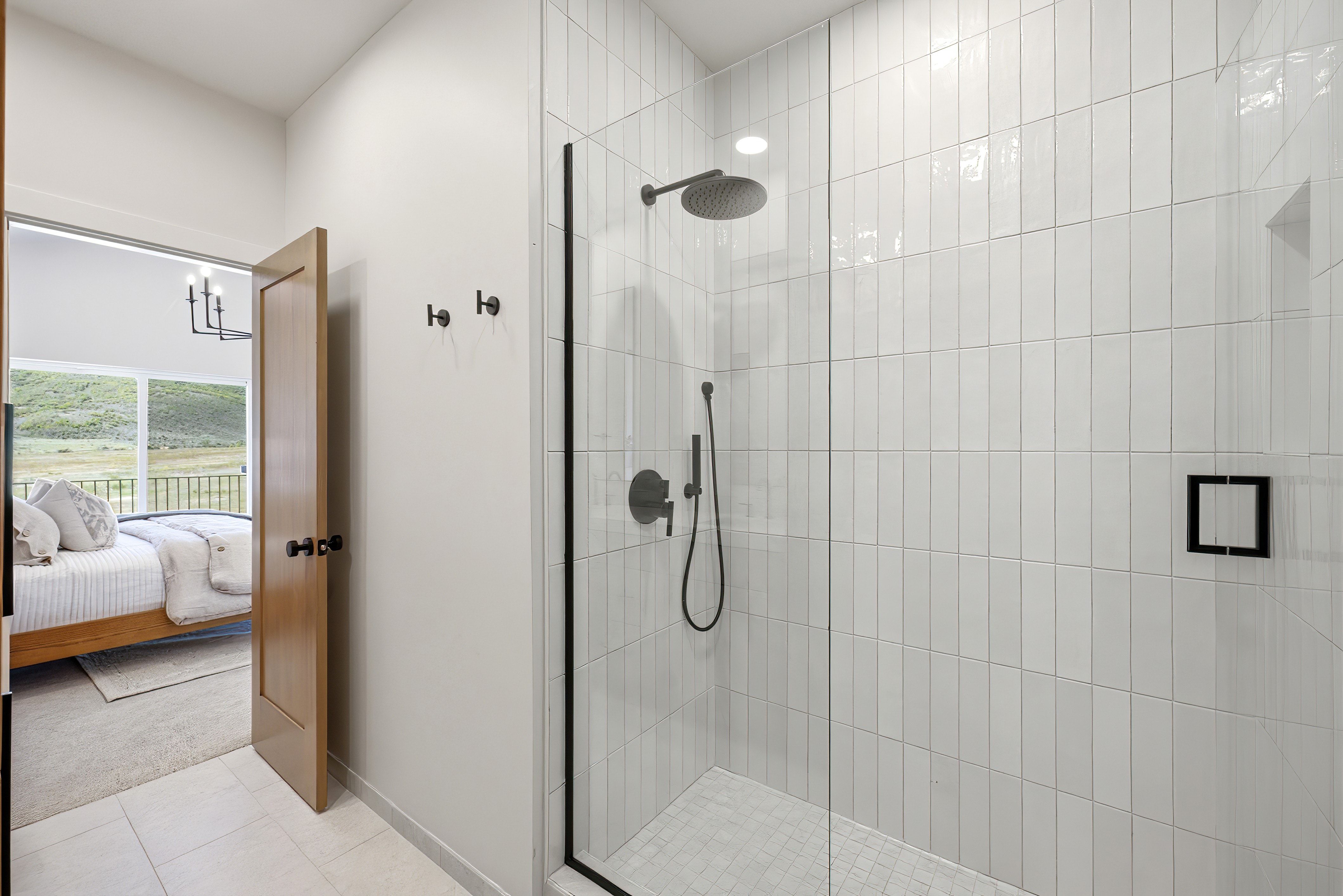 Glass-enclosed shower featuring vertical white subway tile, matte black fixtures, and a recessed shower niche