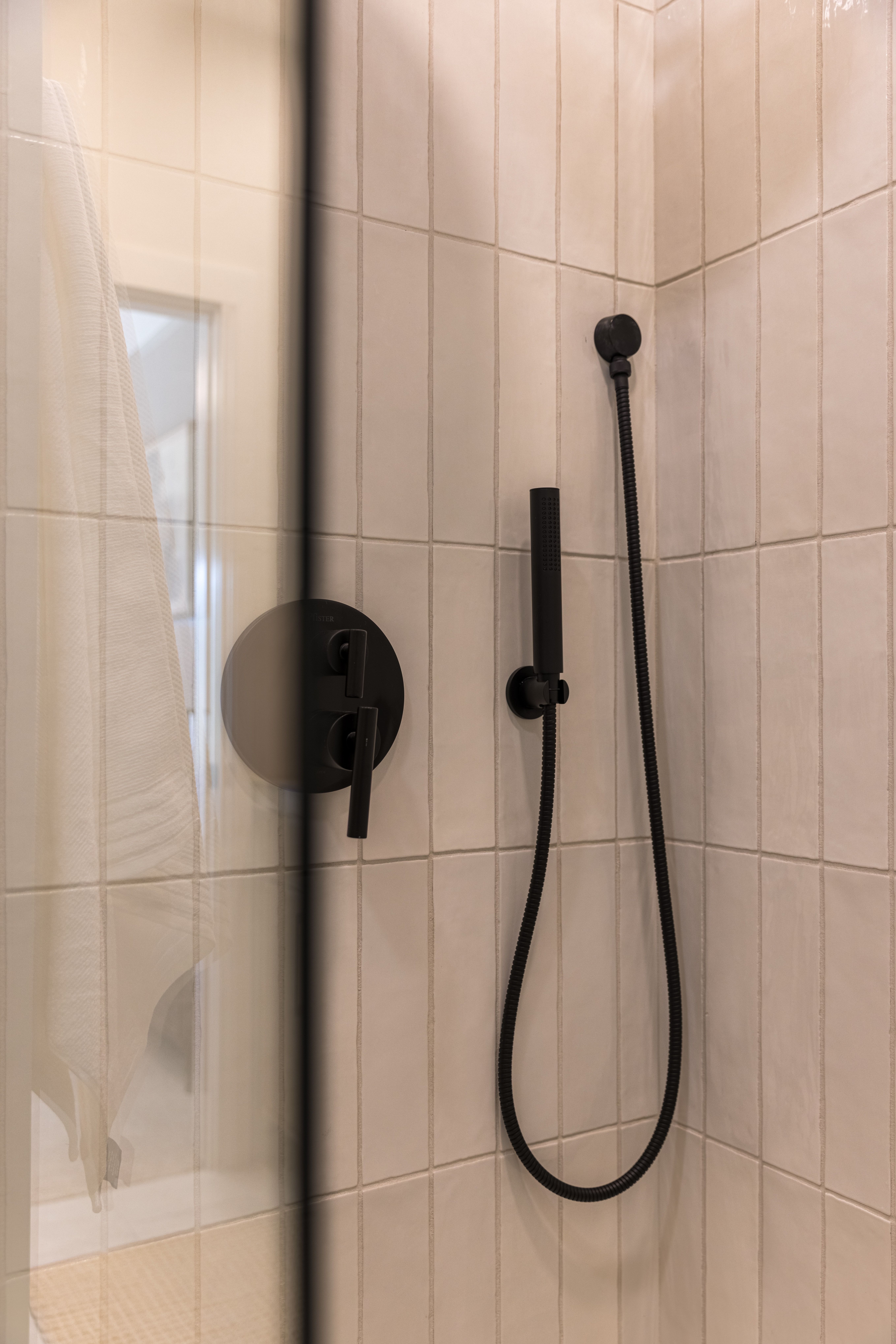 Shower with rectangular light-colored wall tiles, matte black fixtures, and a clear glass enclosure