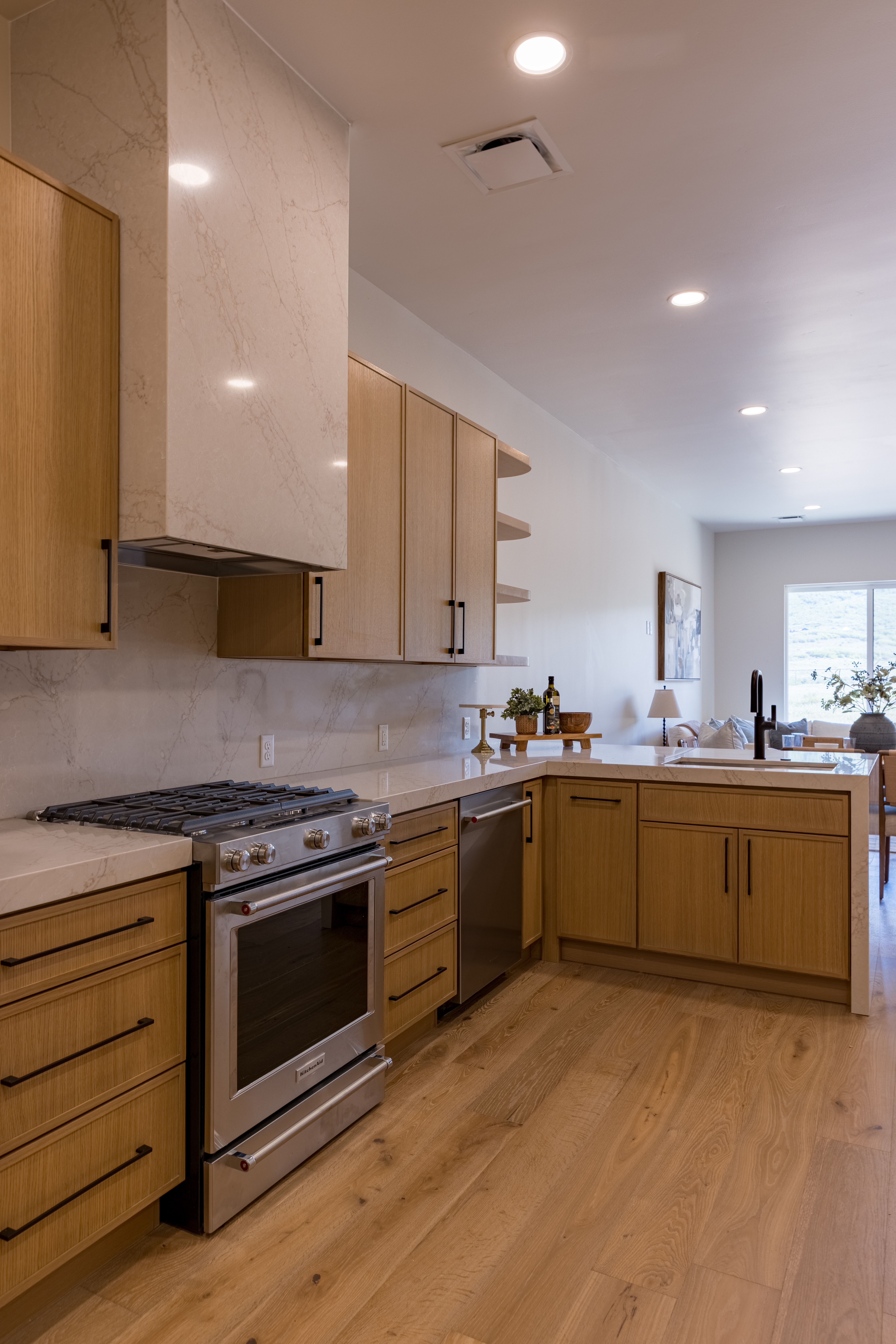 Kitchen featuring wood-finish flooring, light wood cabinetry with dark hardware, stainless steel appliances, and a marble-finish range hood