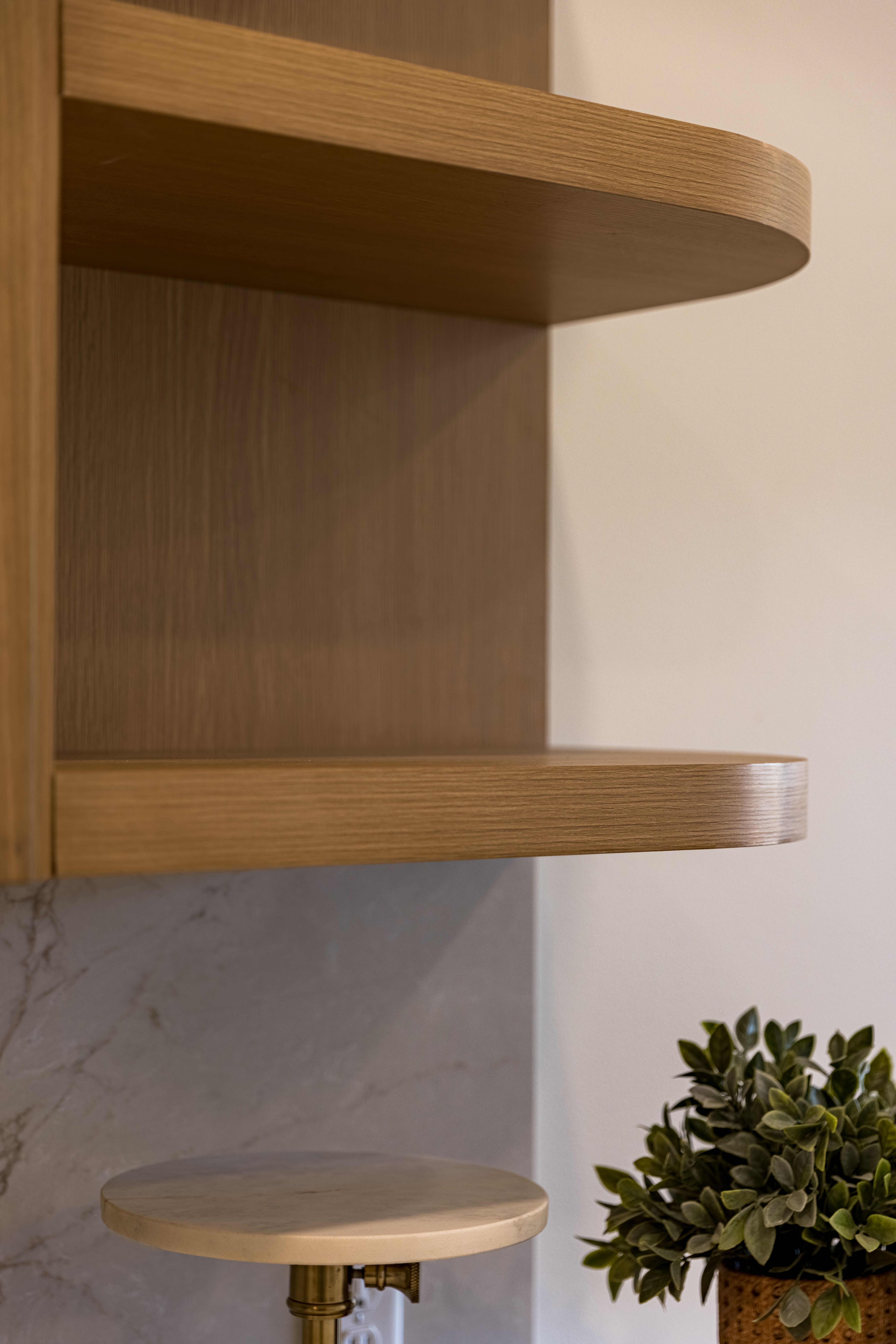 Light wood-finish open shelving with curved edges, set against a white wall and a marble-patterned backsplash