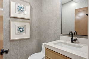 Powder room featuring a wood-finish vanity with a white countertop and integrated sink, matte black faucet, and a contemporary wall-mounted mirror