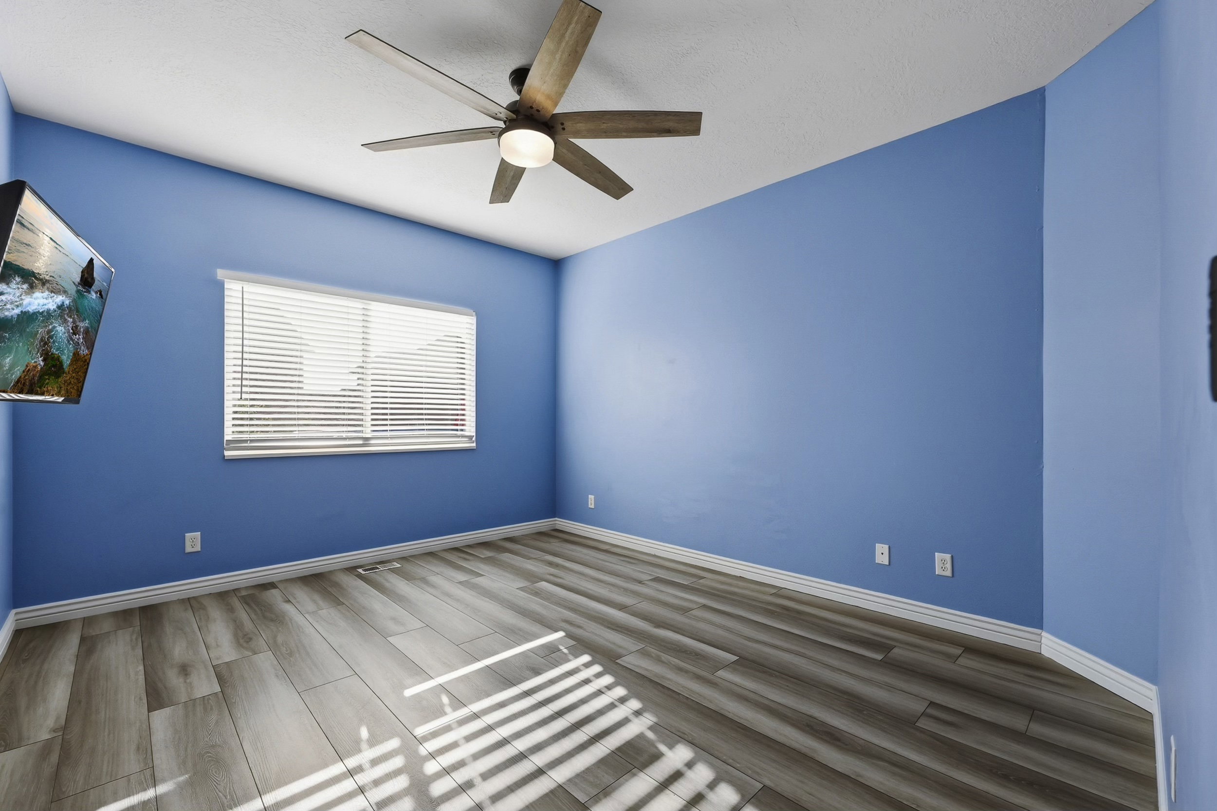 Room featuring wood-finish flooring, a ceiling fan with integrated lighting, and a window with horizontal blinds