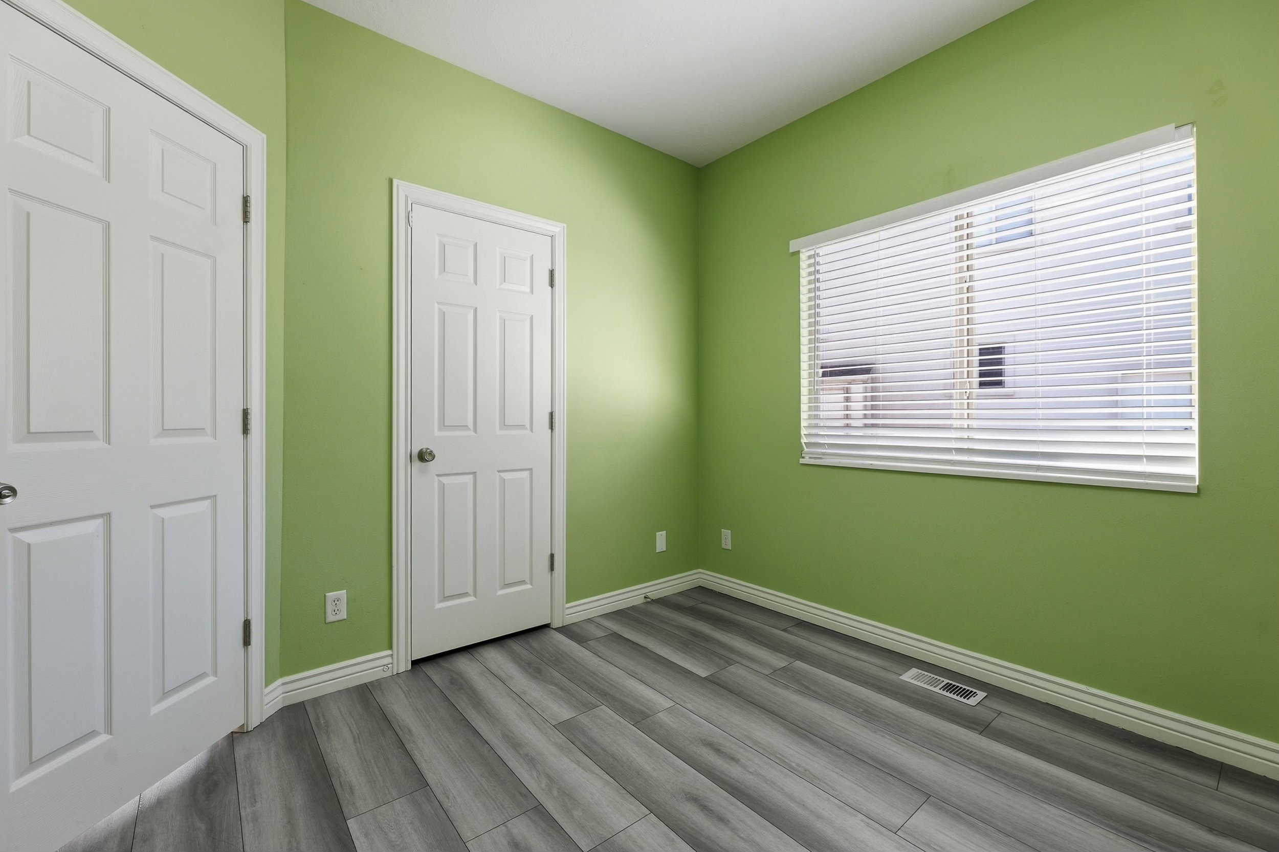 Room featuring wood-finish flooring, two white panel doors, and a window with horizontal blinds