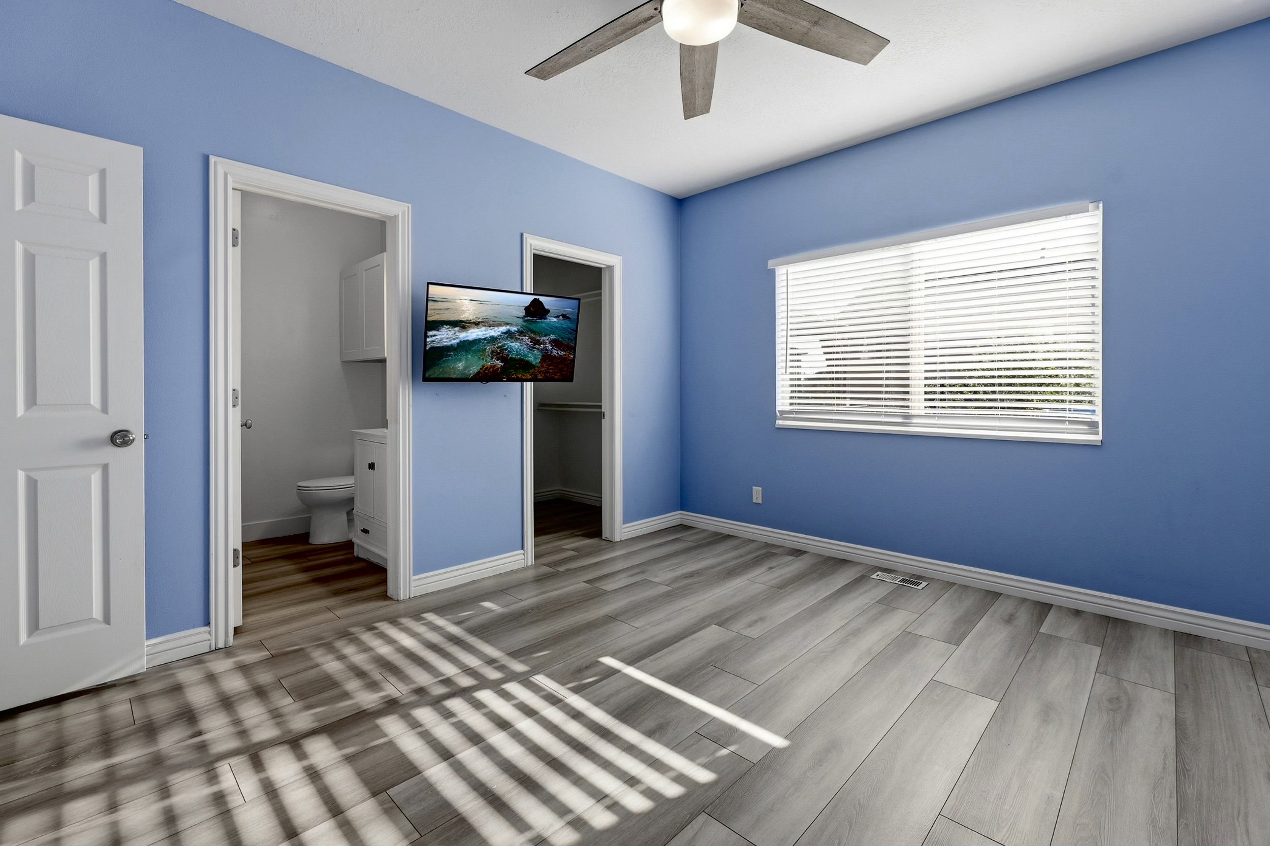 Room featuring wood-finish flooring, a ceiling fan with integrated lighting, and a window with horizontal blinds