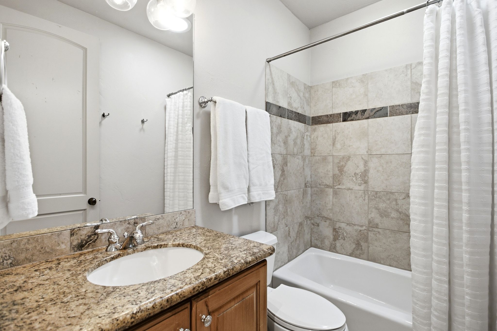 Bathroom featuring a tub/shower combination with tiled surround, a granite-finish countertop, an oval undermount sink, and a wood-finish vanity