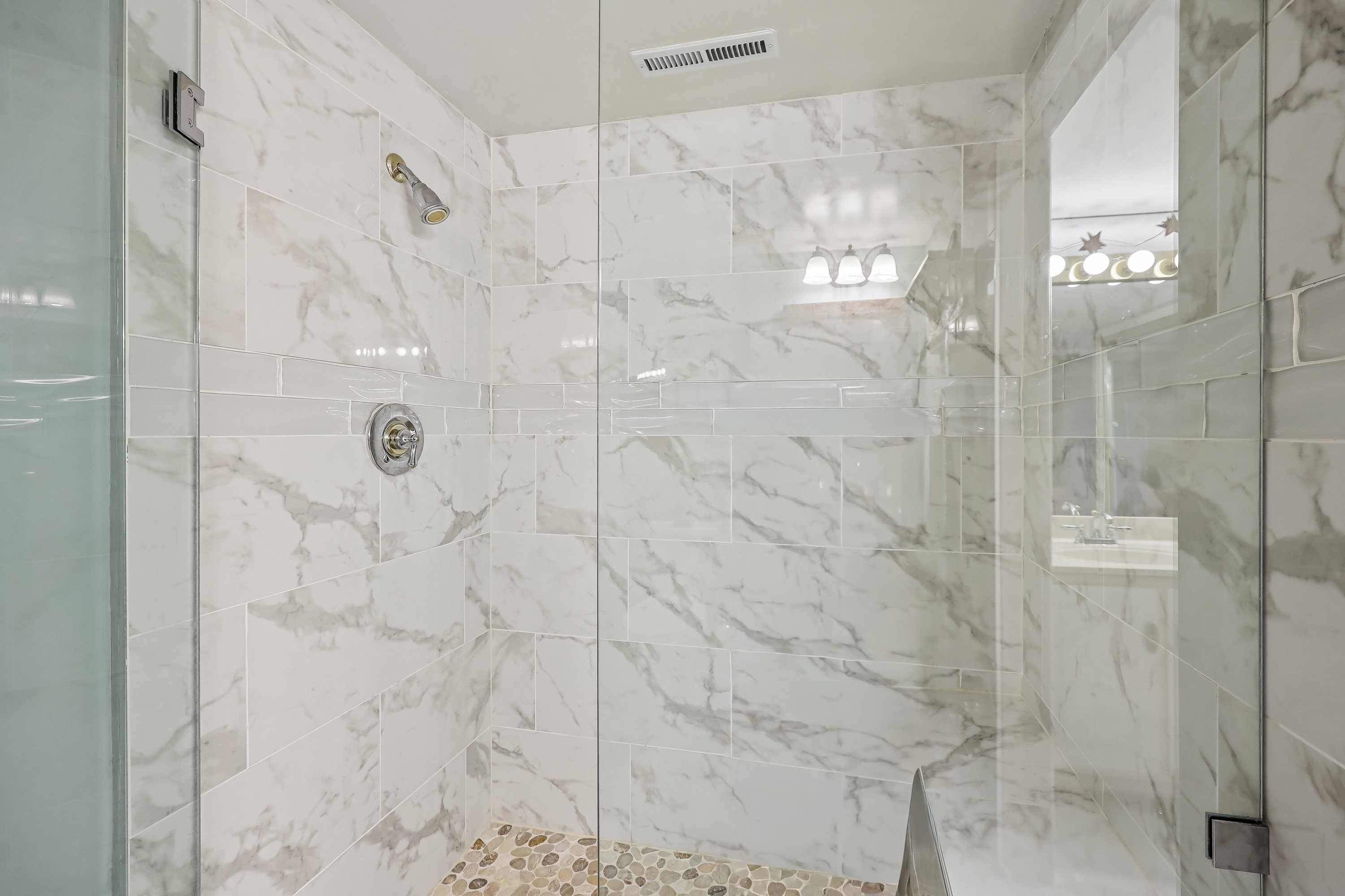 Walk-in shower featuring large format tile walls, a decorative tile accent band, and a pebble-stone floor