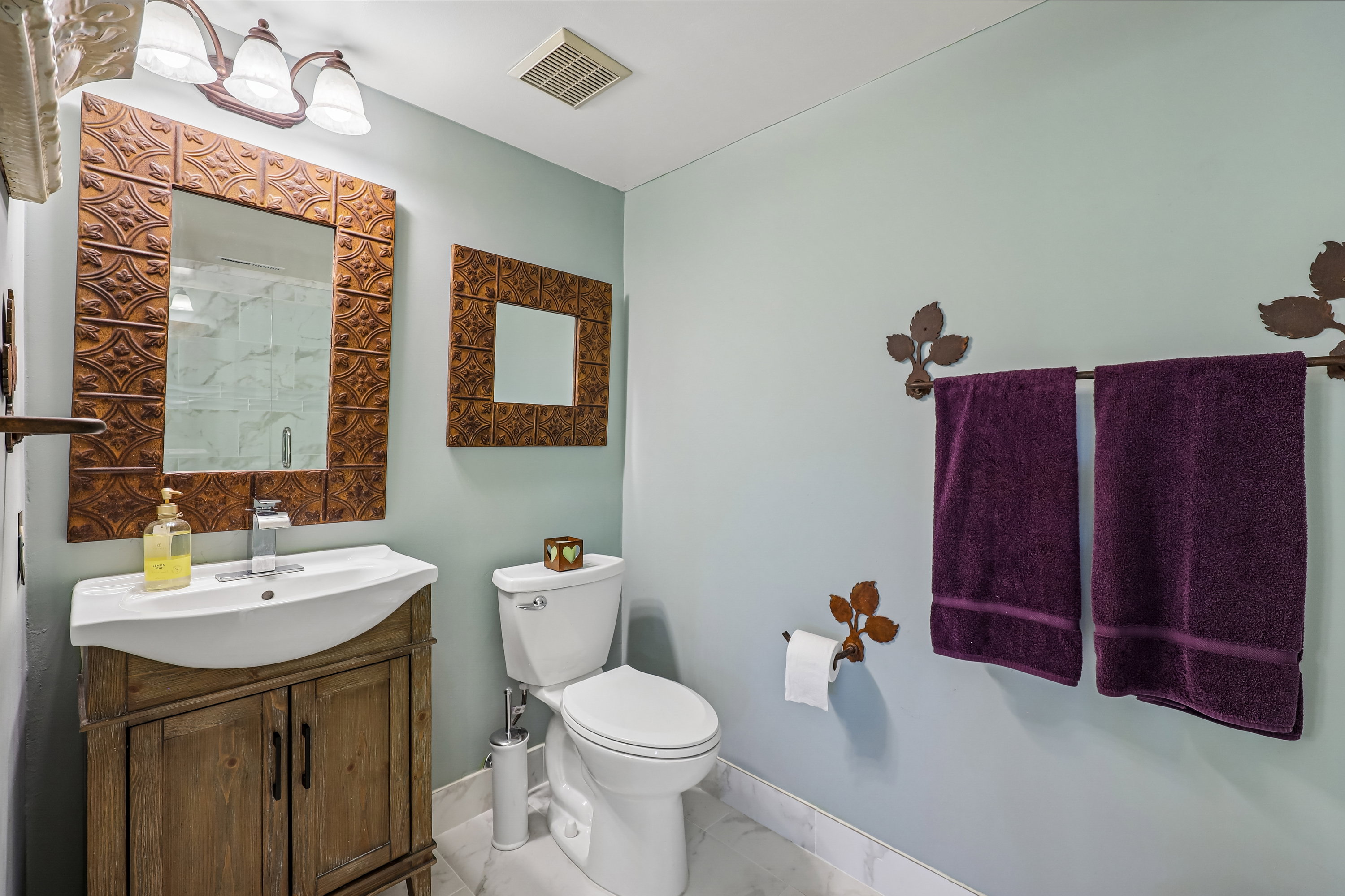 Bathroom featuring a distressed wood-finish vanity with an integrated sink, a rectangular mirror with an embossed frame, and a white toilet
