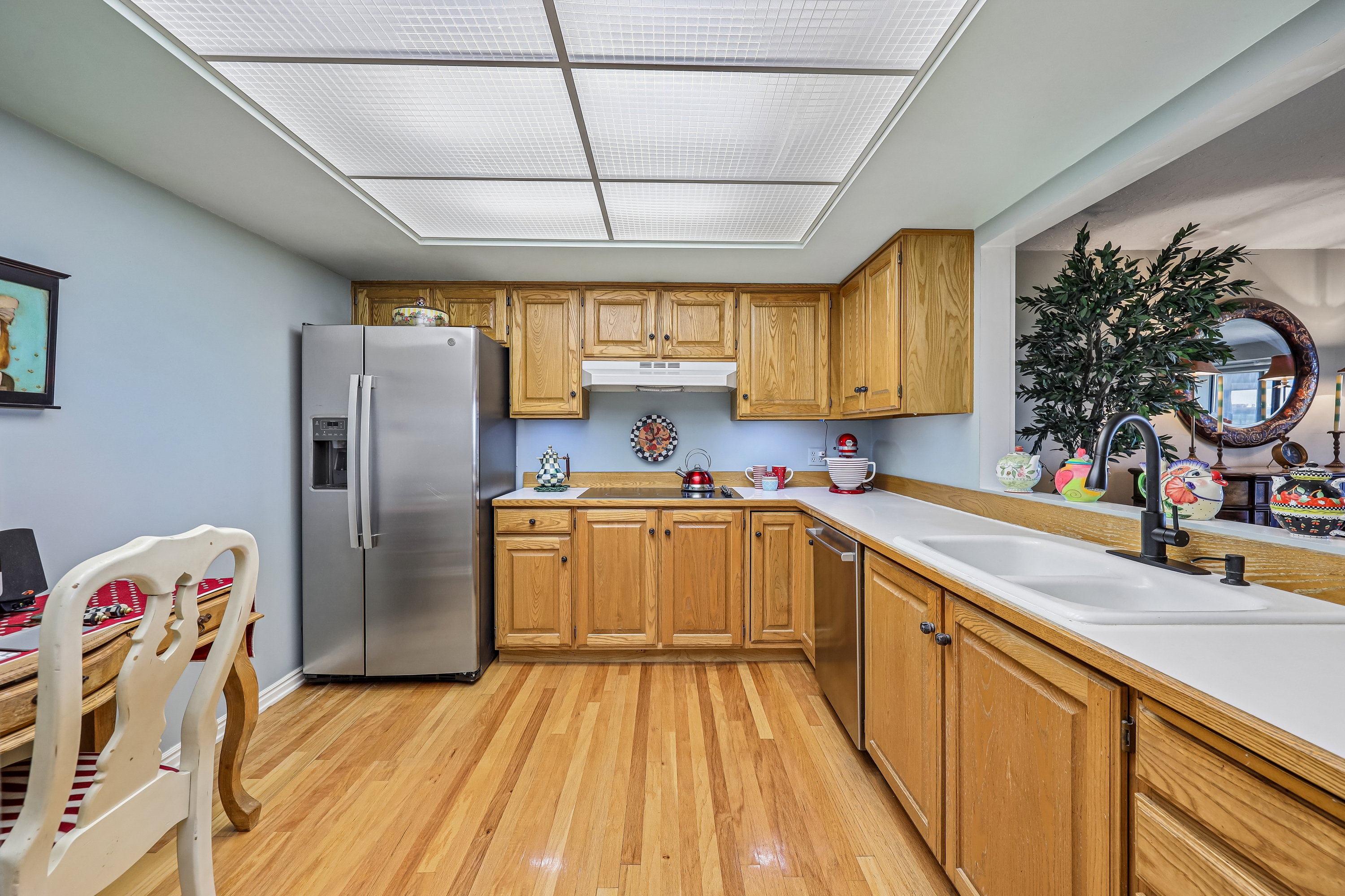 Kitchen featuring natural wood cabinetry, wood-finish flooring, stainless steel appliances, white countertops, and a double basin sink with a matte black faucet