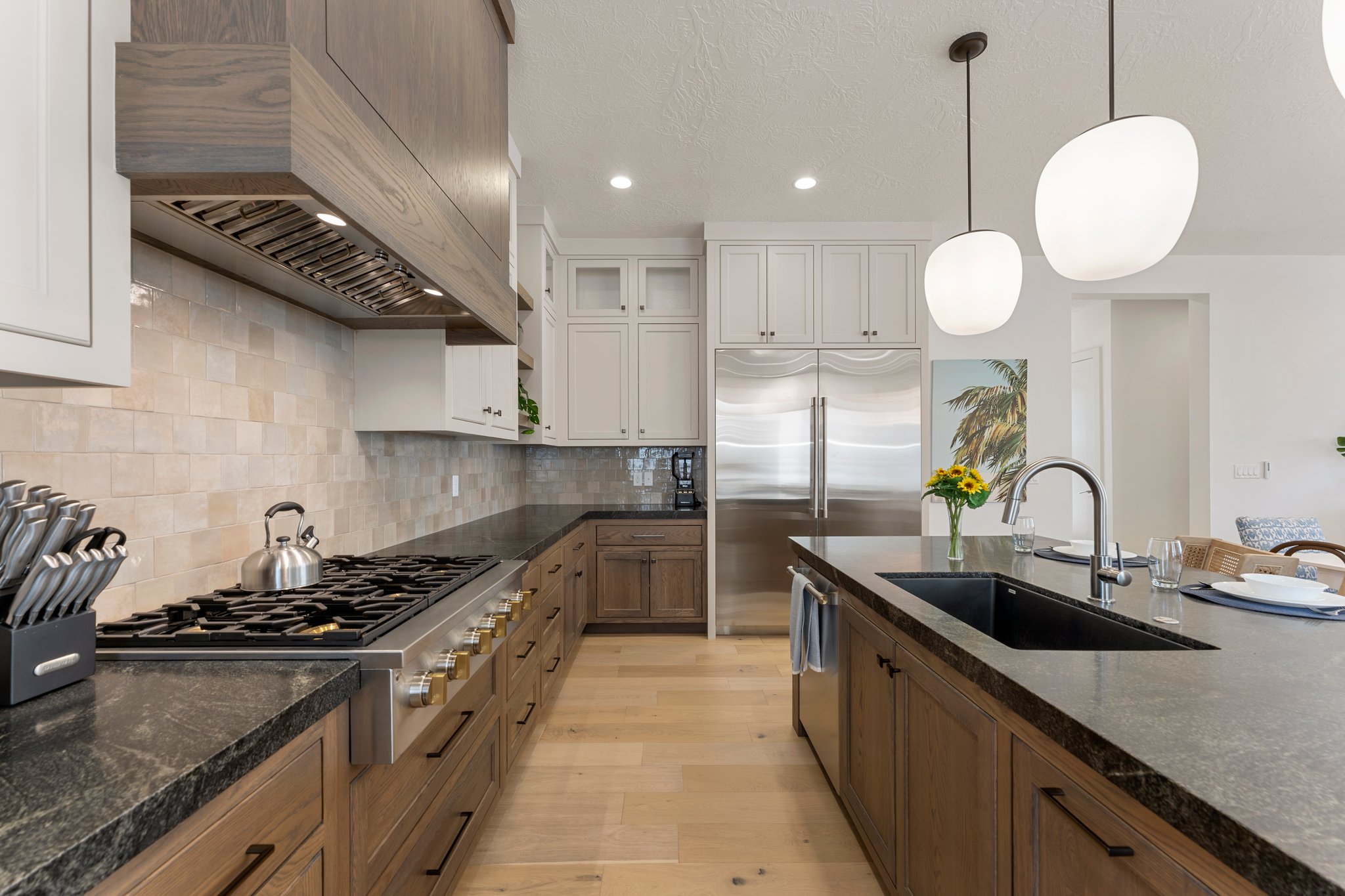 Chef's kitchen featuring a stainless steel range with a custom wood-finish hood, stone countertops, and a full-height tile backsplash