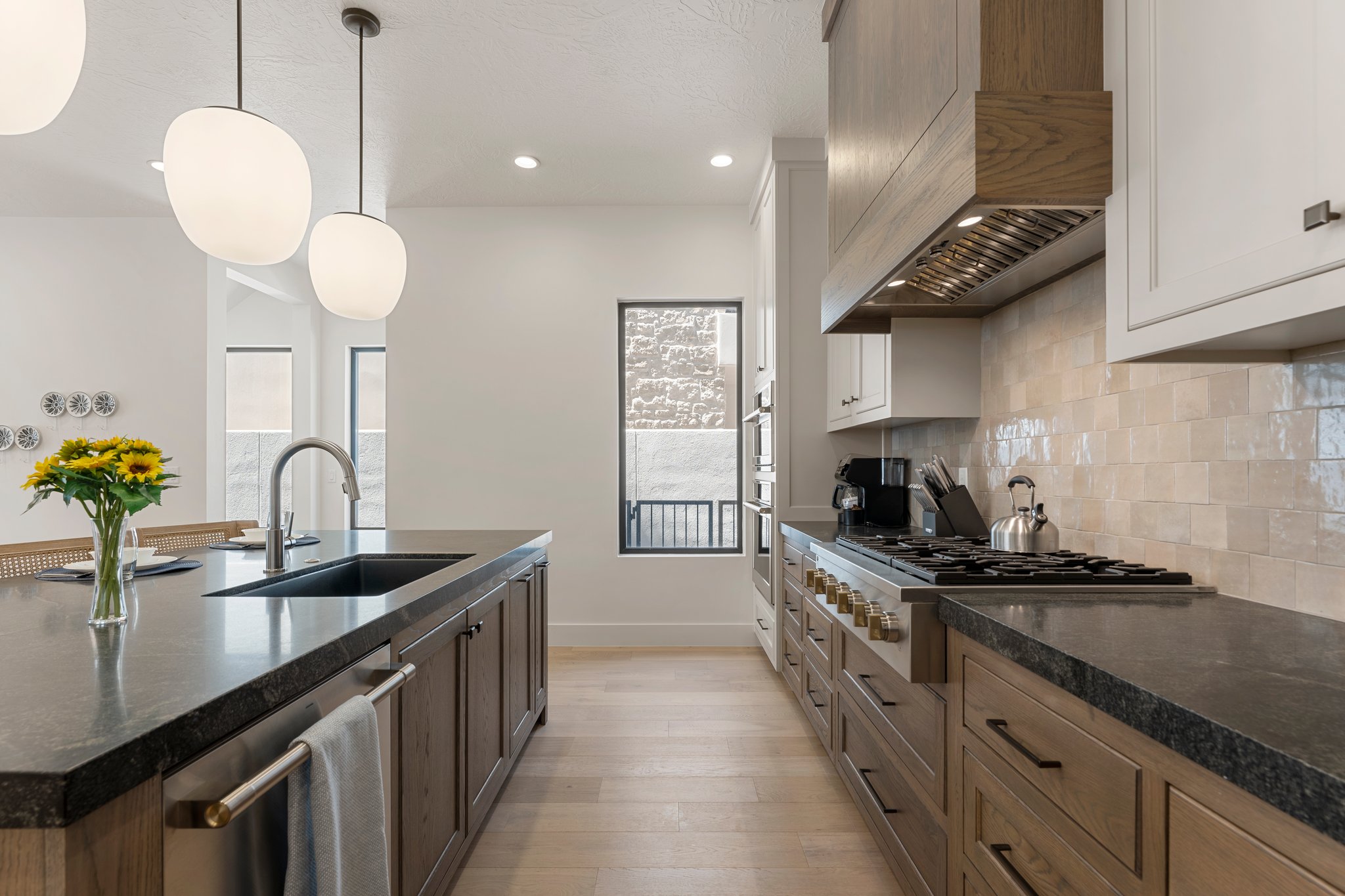 Contemporary kitchen featuring a spacious island with an undermount sink, pendant lighting, professional-grade range, custom wood-finish cabinetry, and light-toned tile backsplash