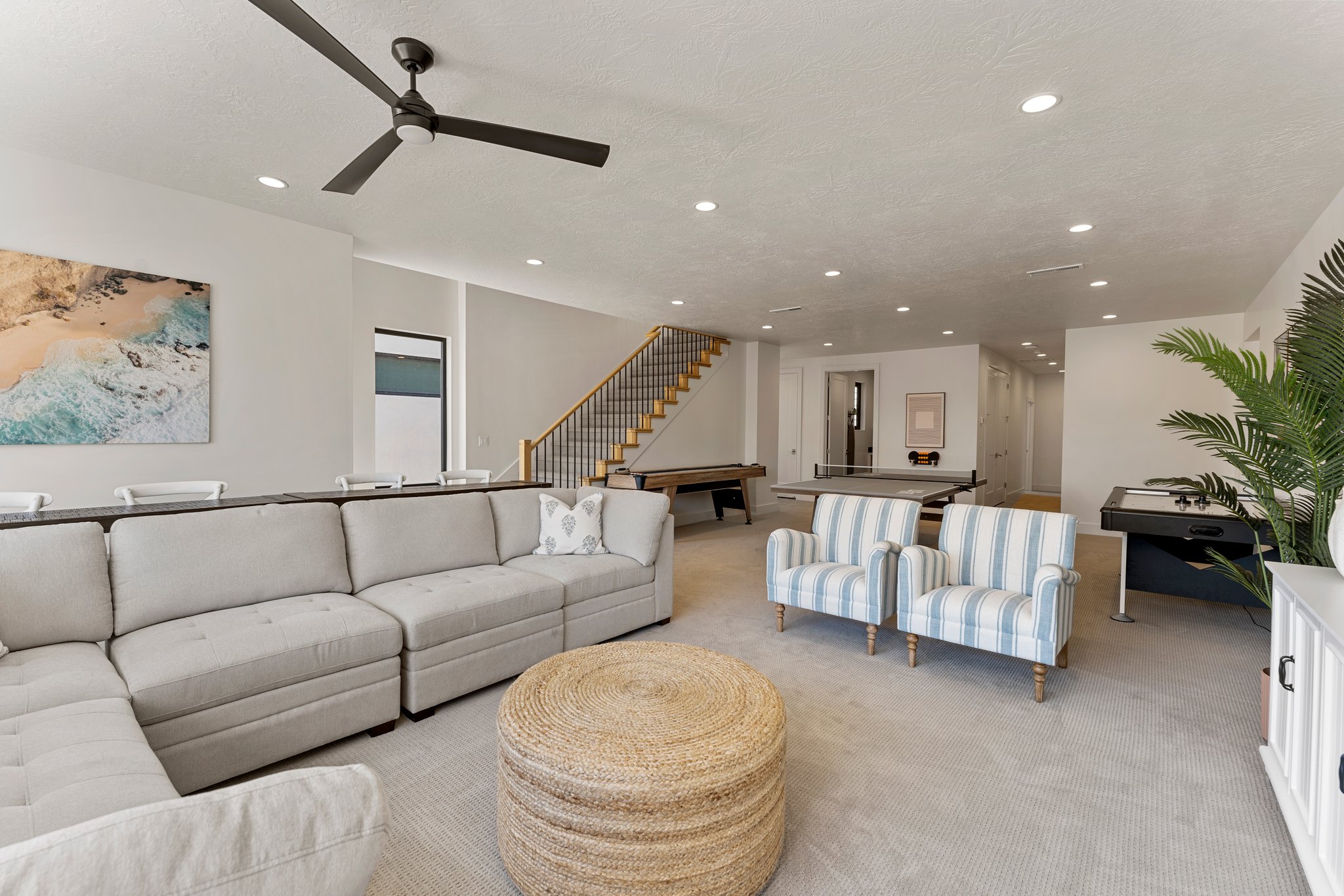 Spacious recreation room featuring recessed lighting, a modern ceiling fan, and a wood staircase with black metal balusters