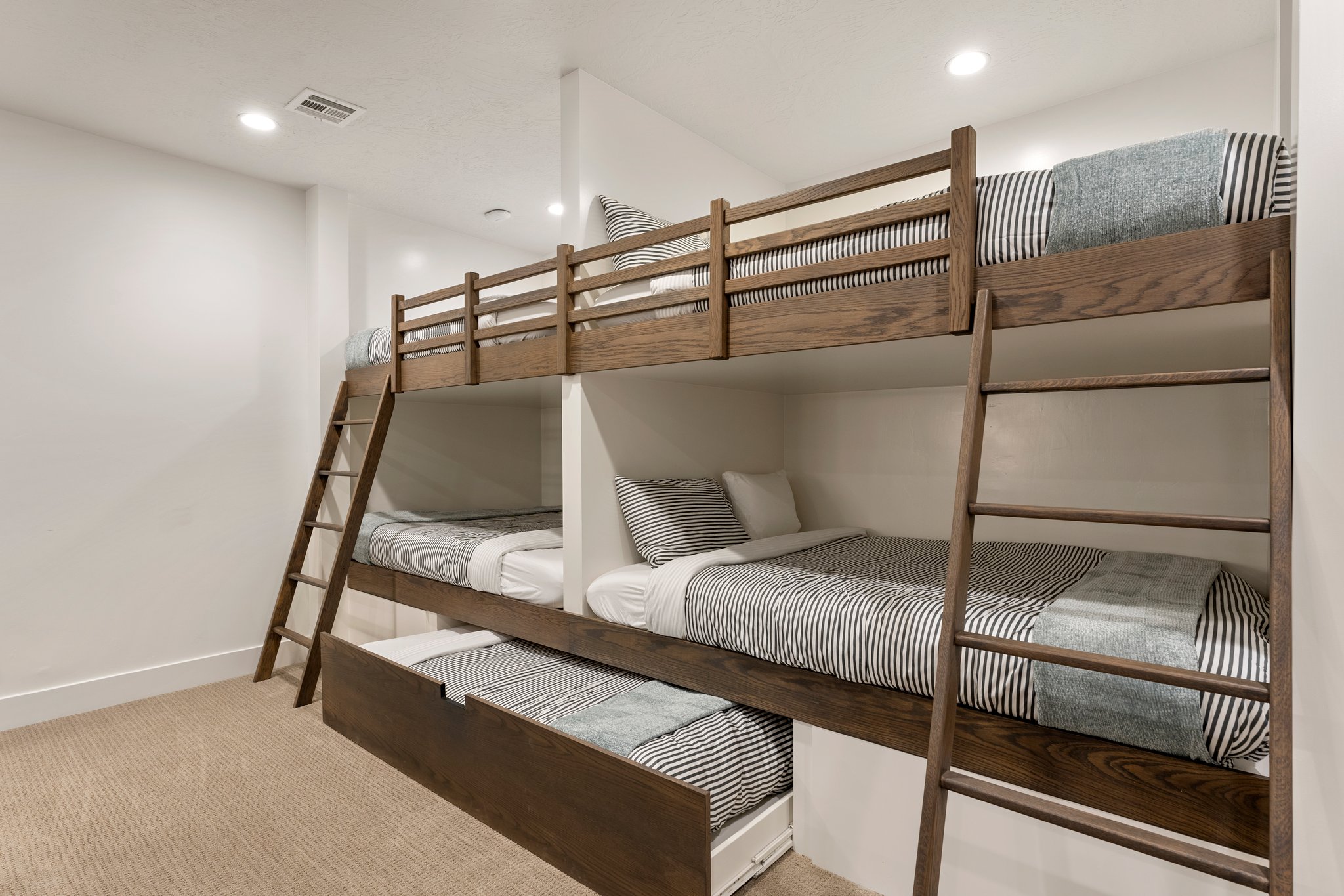 Built-in bunk beds with wood-finish frames, integrated ladders, and a pull-out trundle bed
