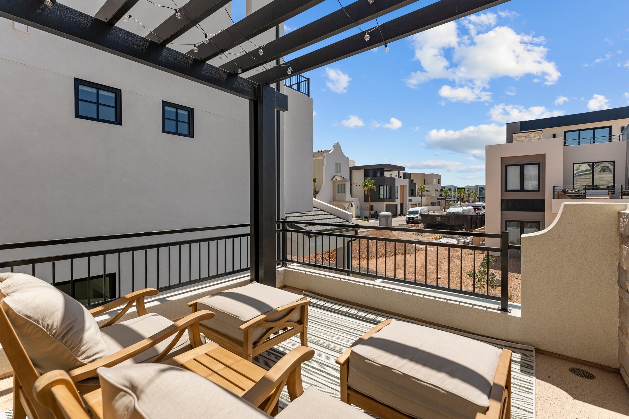Covered outdoor patio featuring a black pergola with string lights, iron railings, and a striped area rug